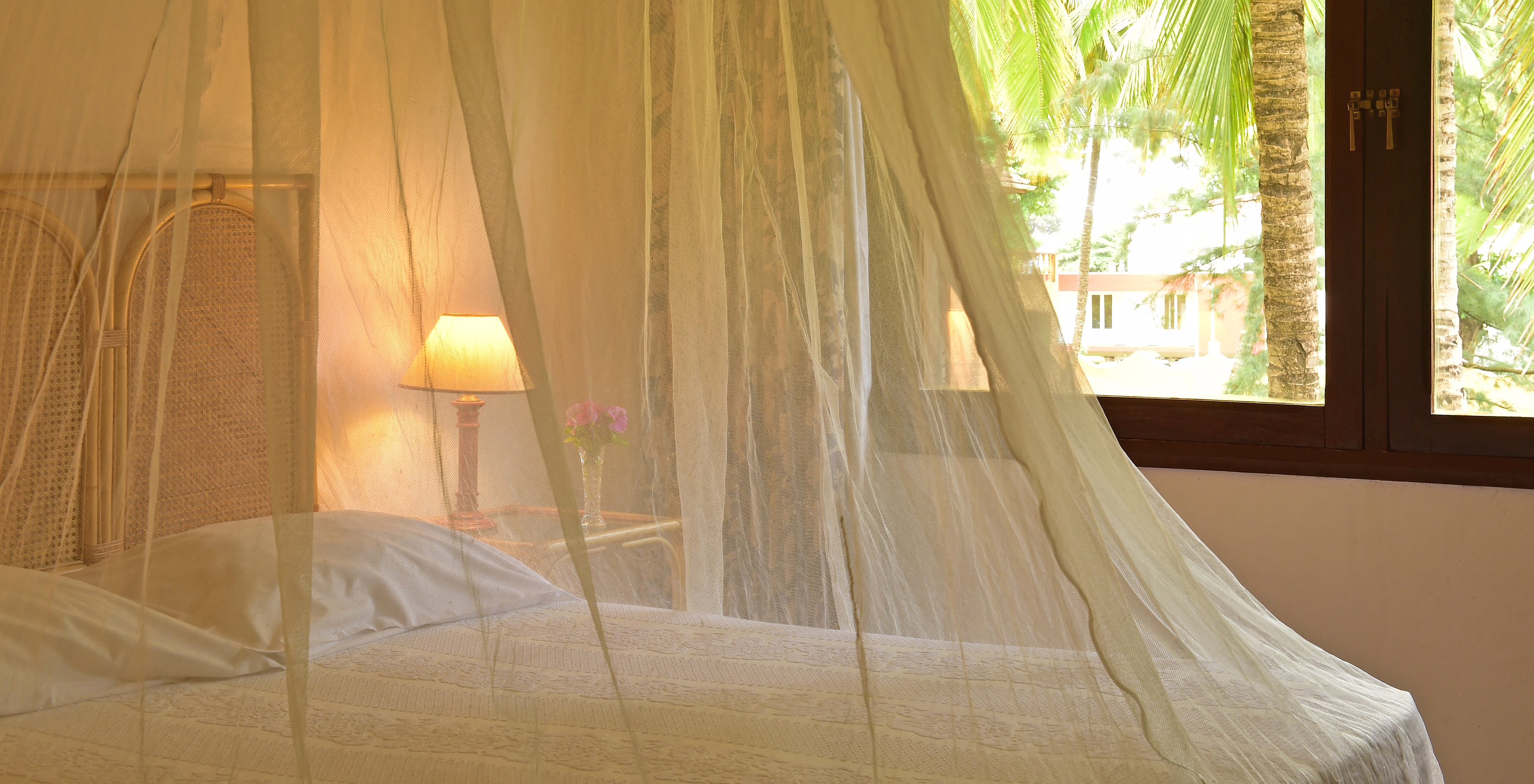 La Junior Suite del Pestana Miramar São Tomé tiene una cama matrimonial con mosquitero y una ventana con vista al jardín