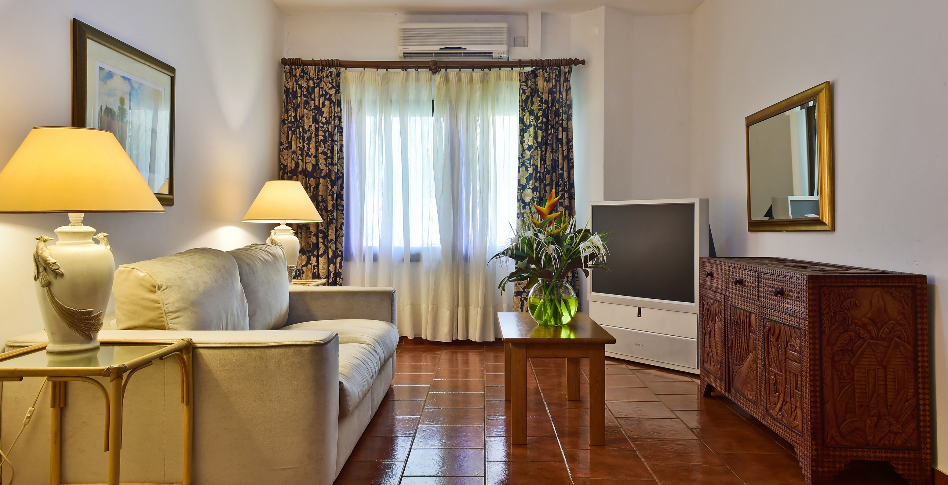 La Suite del Pestana Miramar São Tomé tiene una sala de estar con sofá, televisor y una mesa con un jarrón de flores