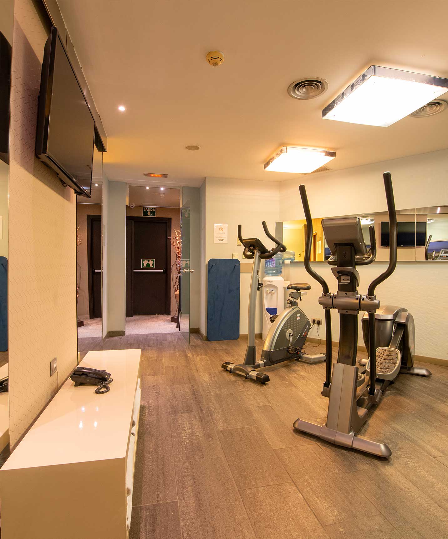 El hotel en Barcelona tiene un centro de fitness para sus clientes con varias máquinas, un espejo y una televisión