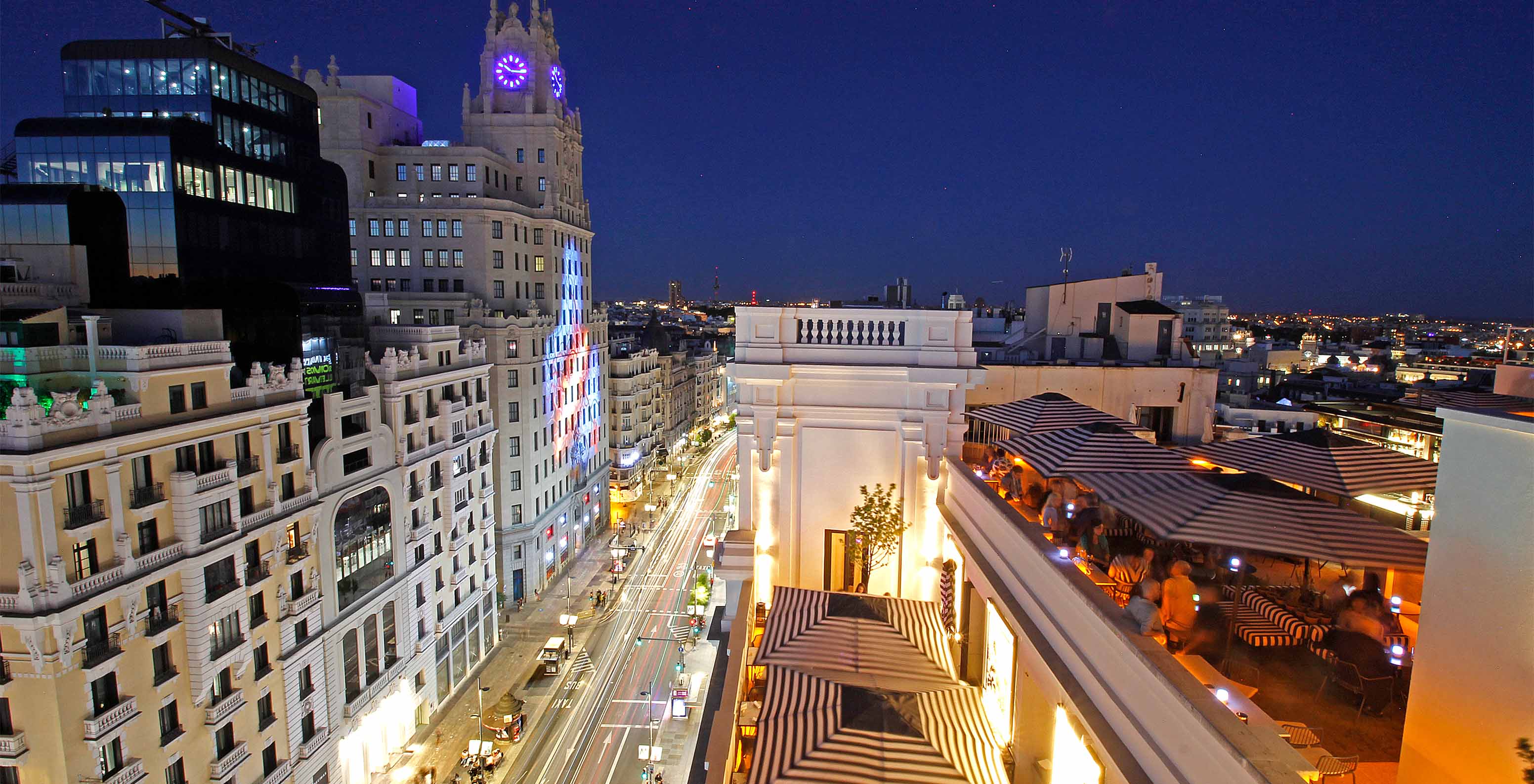 Restaurante del hotel en el rooftop con mesas, sillas y vista a los edificios de la Gran Vía