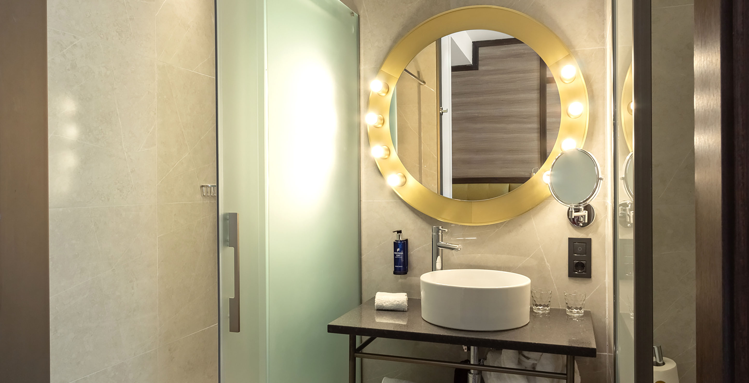 El Premium del Pestana CR7 Gran Vía Madrid tiene un baño con un espejo y luces, lavabo y puertas de vidrio corredizas