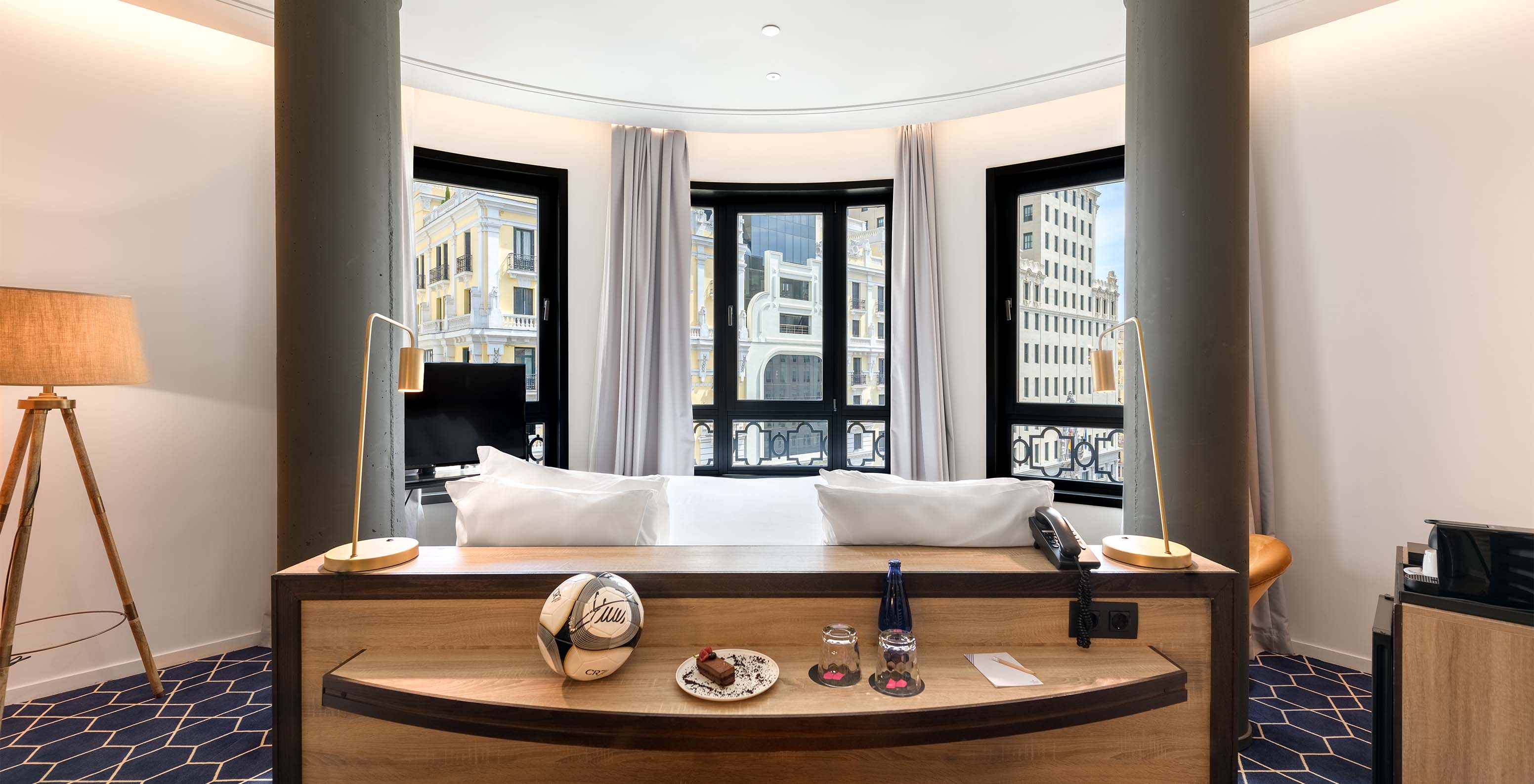 El Deluxe Grand con Vista del Pestana CR7 Gran Vía Madrid tiene una cama doble orientada hacia las ventanas en pared curva