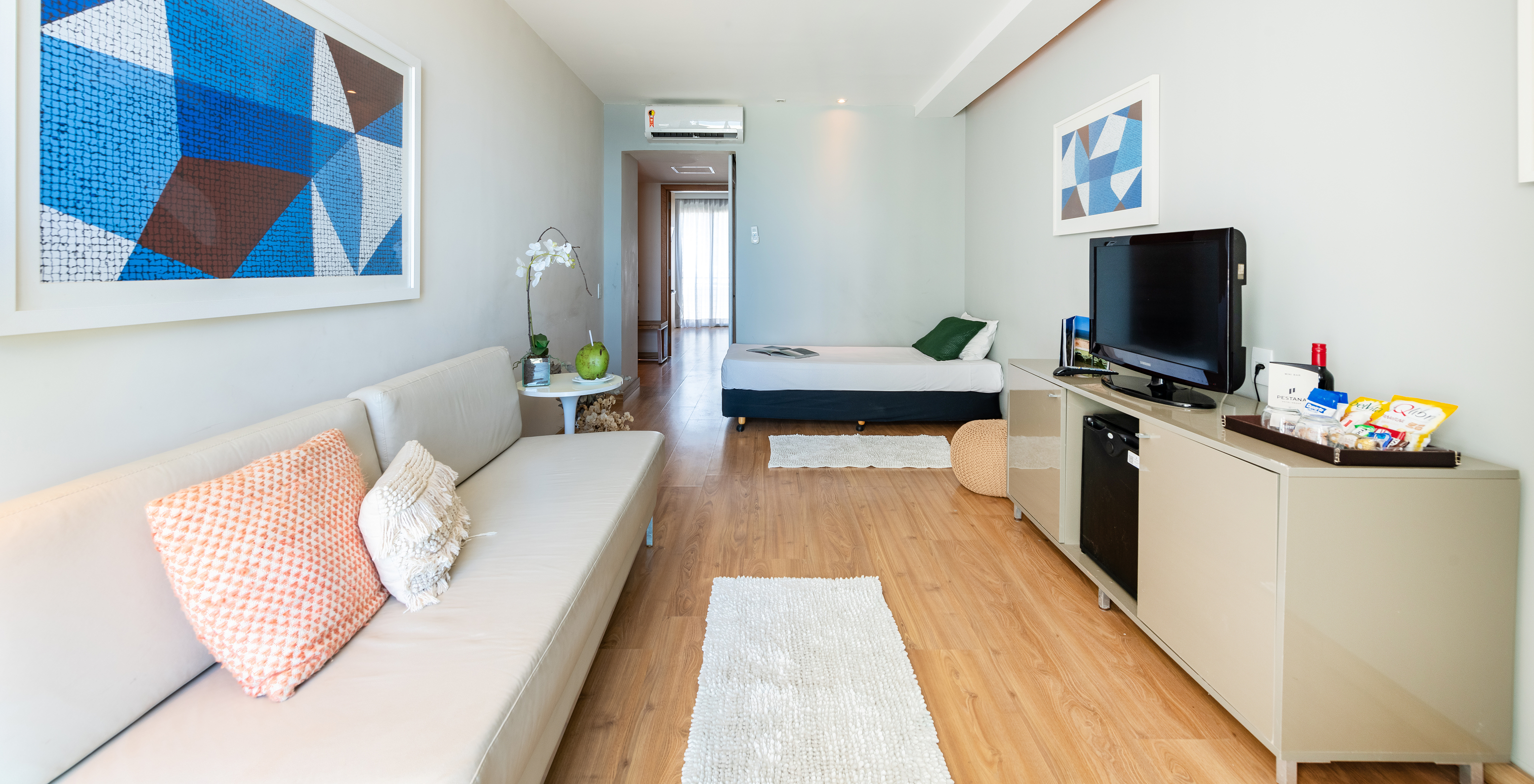 La Suite Vista Mar Lateral del Pestana Rio Atlântica tiene una sala con sofá, cama, una televisión y un cuadro azul