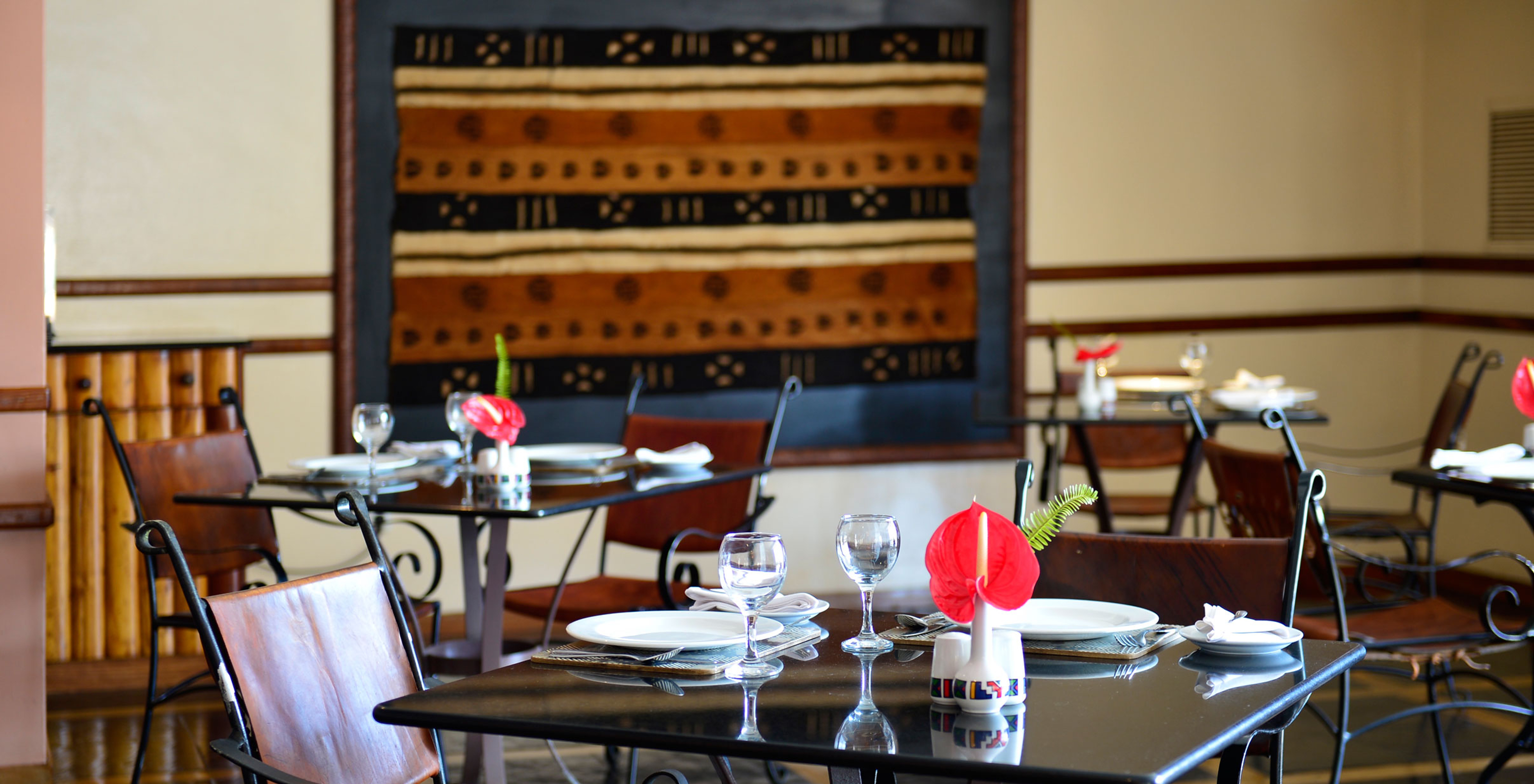 Restaurante en hotel en el centro de Maputo con varias mesas con platos cubiertos y copas y un cuadro africano al fondo