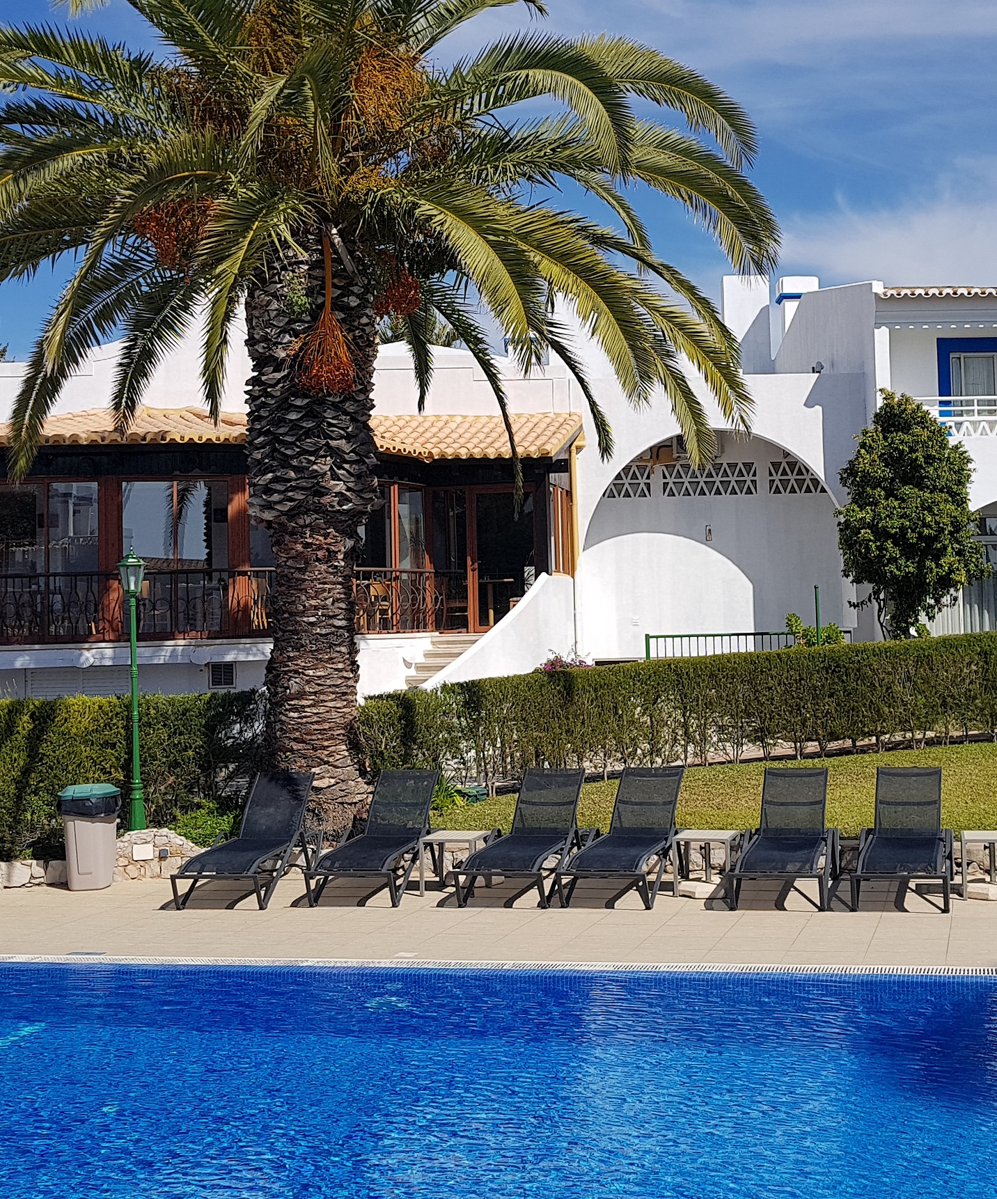 Piscina exterior en el hotel en Carvoeiro, Pestana Palm Gardens, con tumbonas, una palmera y el restaurante detrás