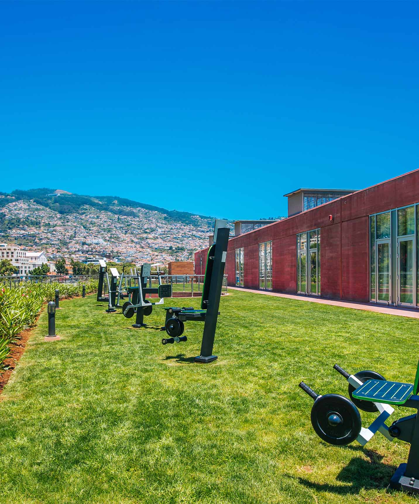 Gimnasio exterior del hotel en el centro, con vista a Funchal, con varias máquinas y un césped verde