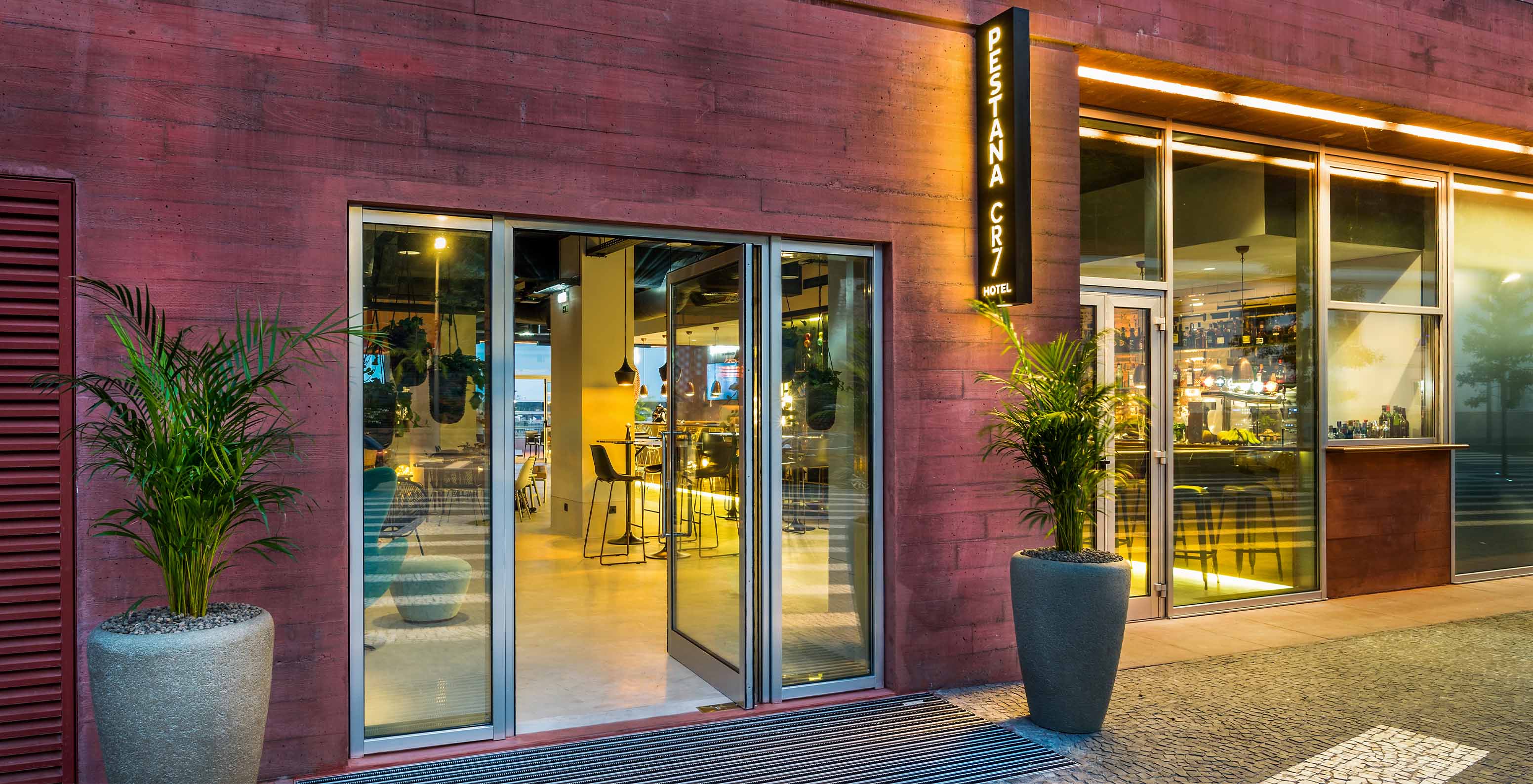 Entrada del hotel en el centro de Funchal con edificio en tonos rosas y una gran puerta de vidrio