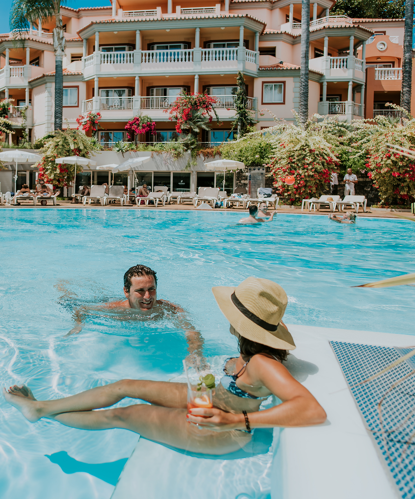 Pareja en la piscina, conversando y bebiendo cócteles, en el Pestana Miramar, un hotel en Madeira cerca de la playa