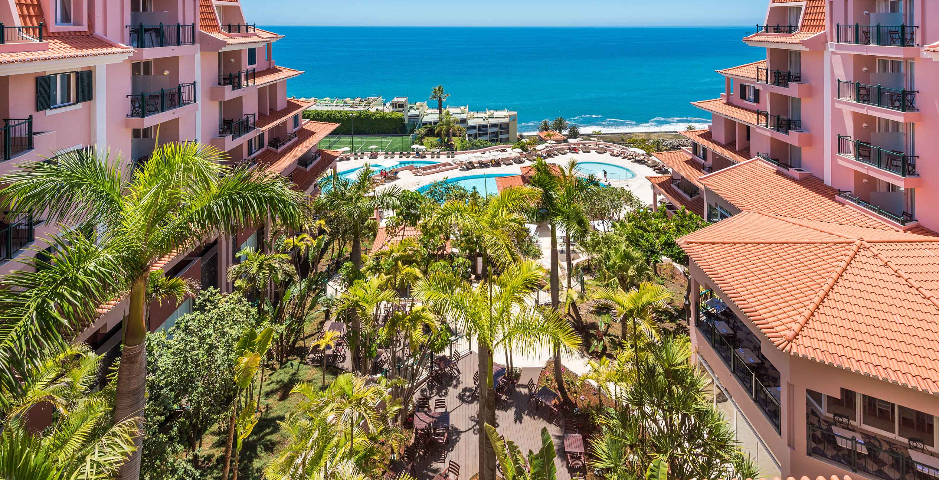 Vista del Pestana Royal All Inclusive, con edificios rosados, una piscina y el océano al fondo