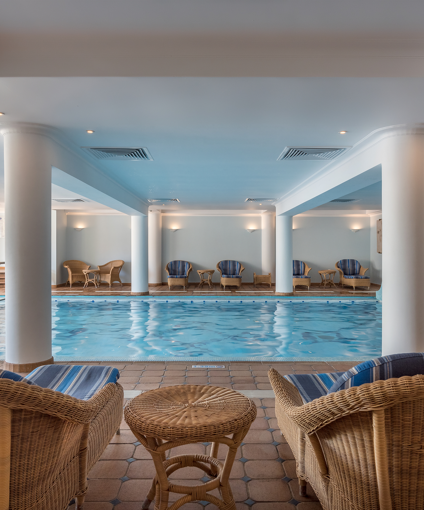 Piscina interior climatizada, con sillas de bambú, del Pestana Village, un hotel romántico en Funchal