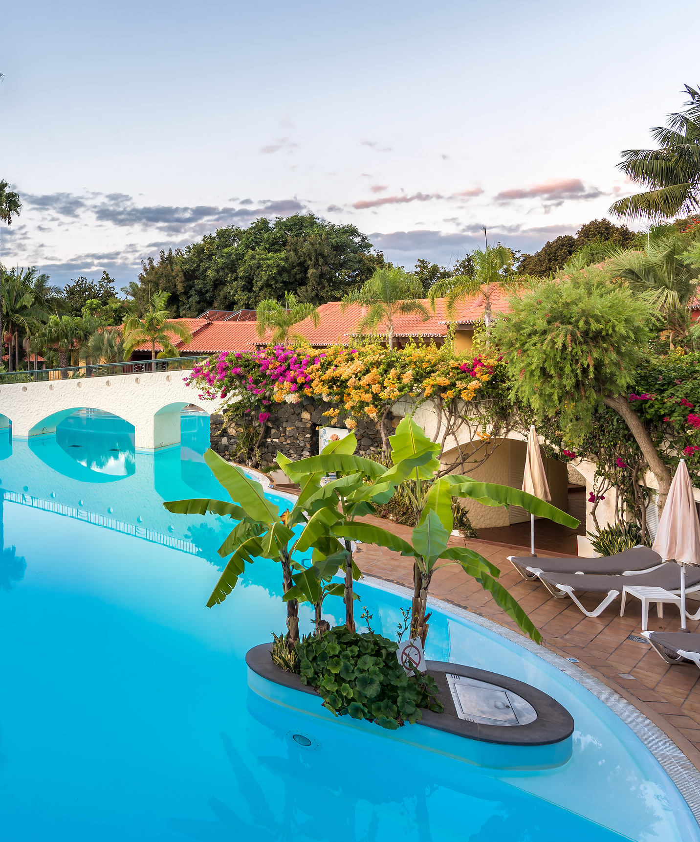 Piscina del Pestana Village, un hotel romántico en Funchal, rodeada de árboles y tumbonas