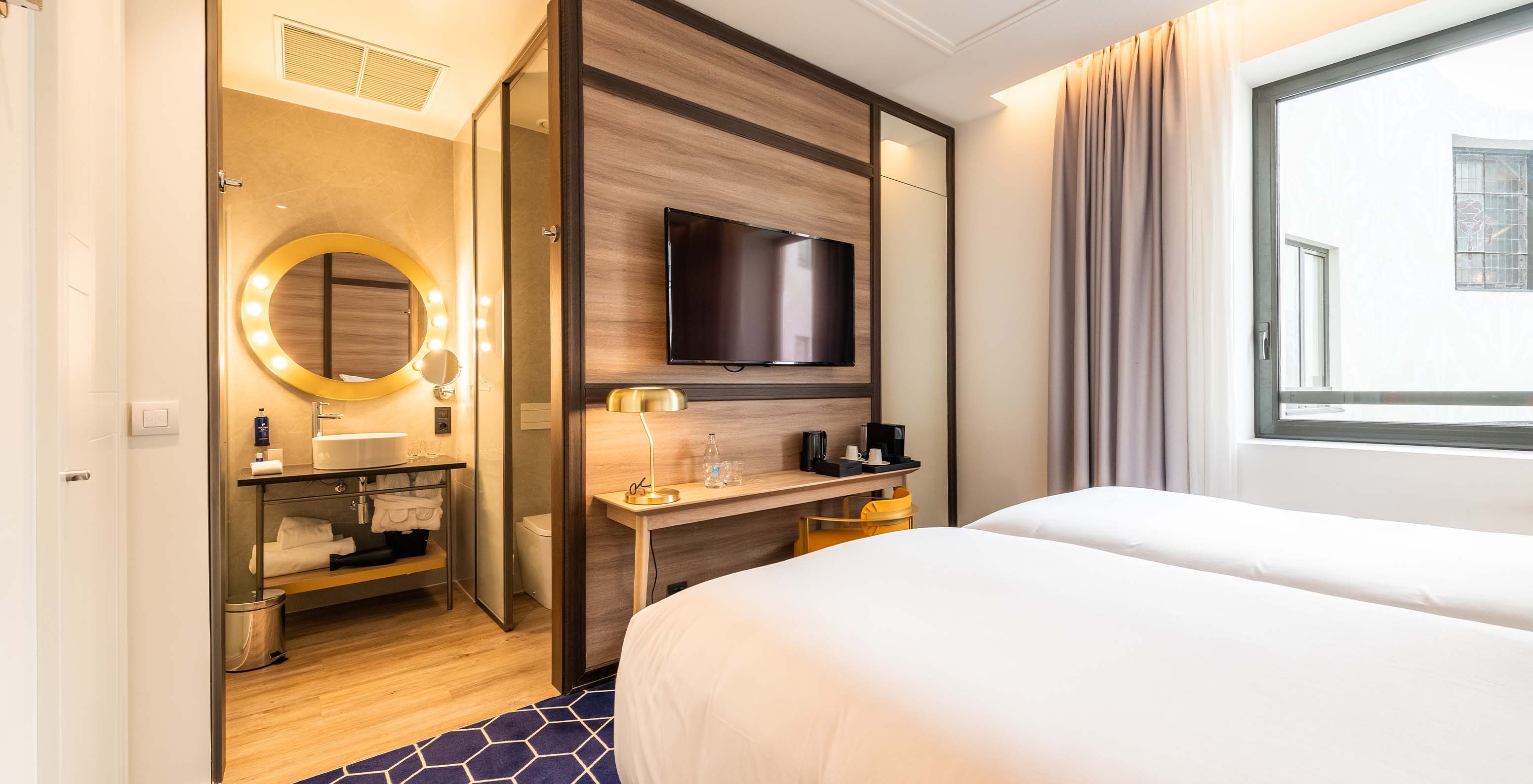 El Cozy Room del Pestana CR7 Gran Vía Madrid tiene dos camas juntas y baño frente con un espejo de luces