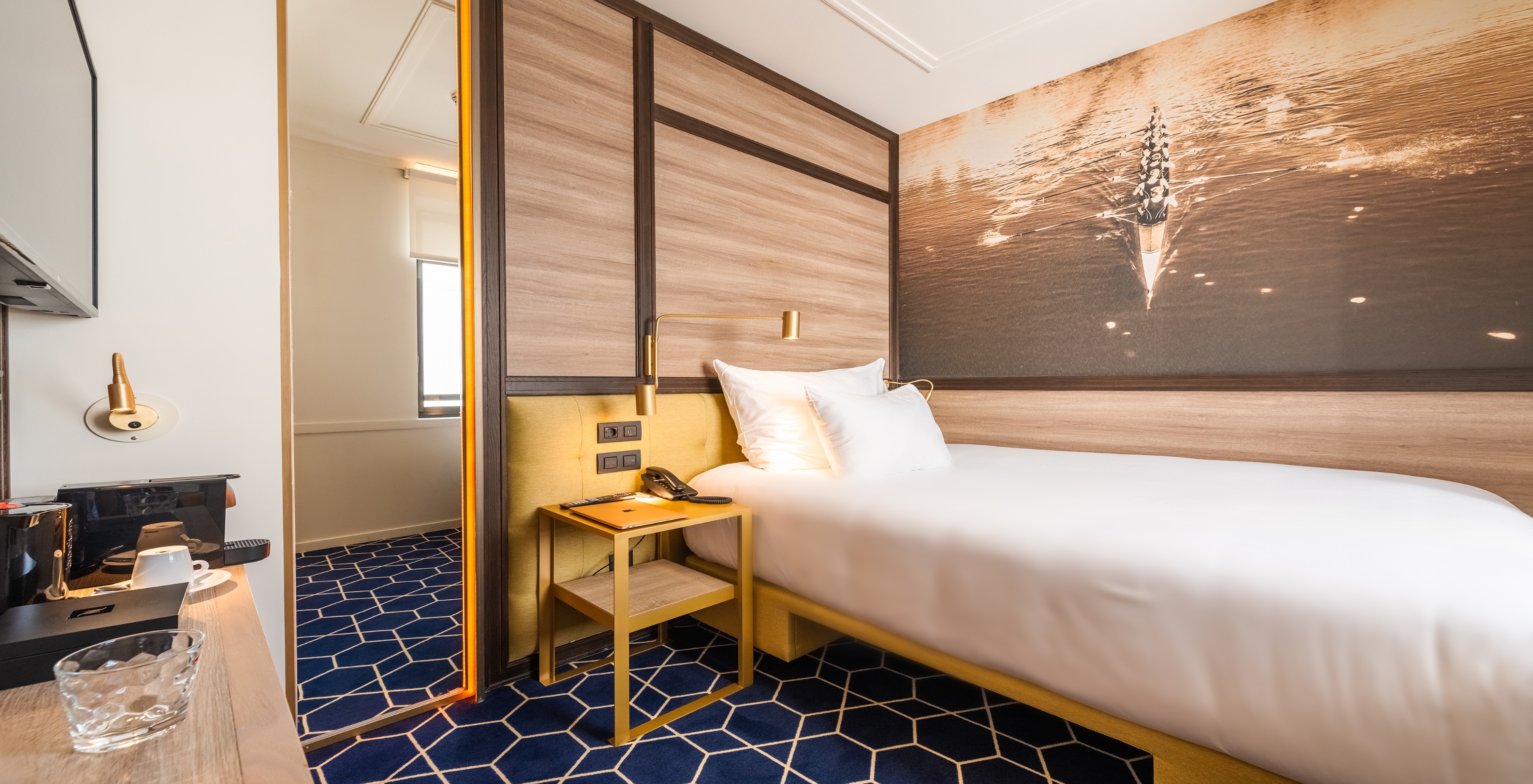 La Cozy Room del Pestana CR7 Gran Vía Madrid tiene una cama junto a la pared y un cuadro en la pared de un equipo de remo