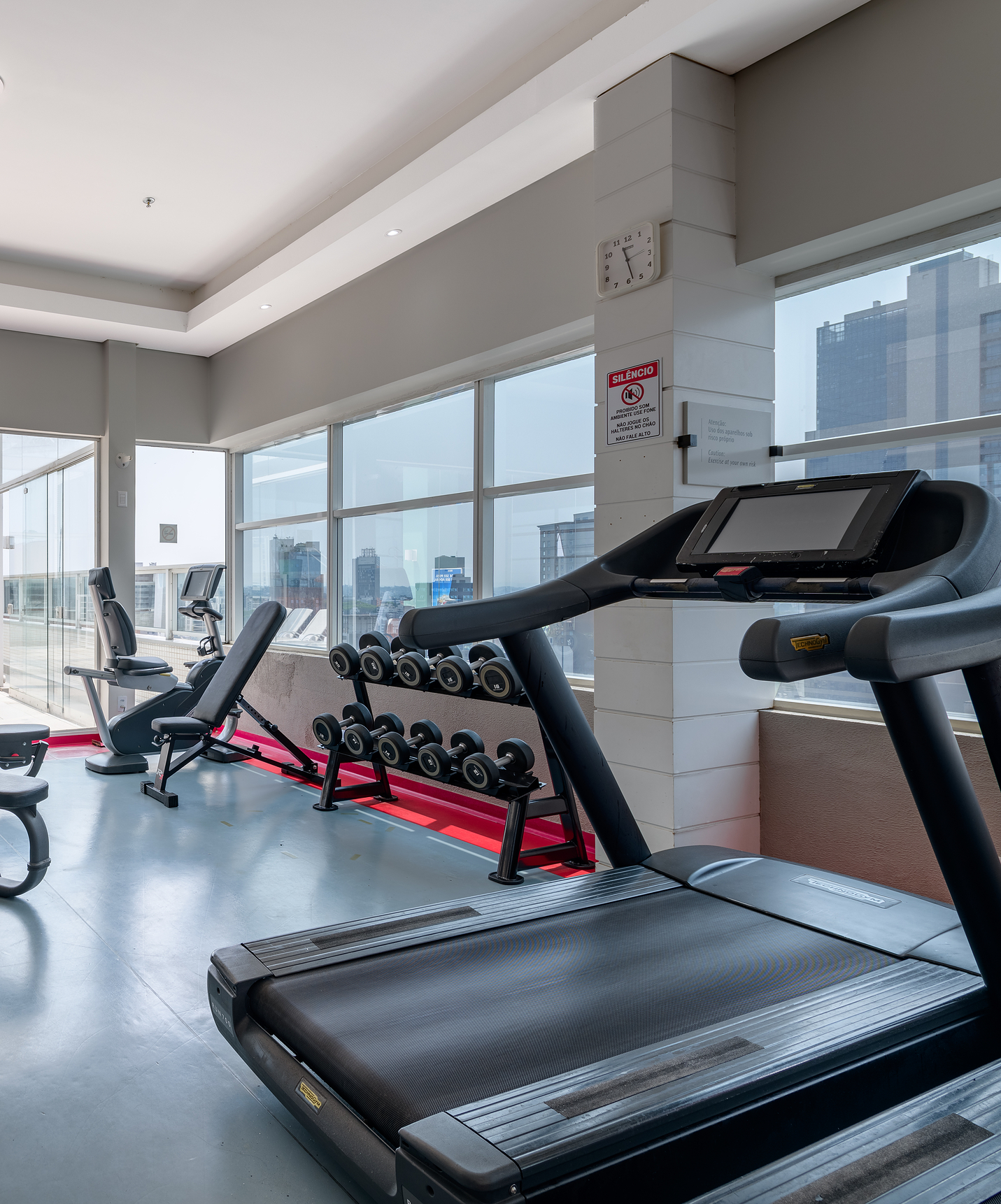 Salle de sport du Pestana Curitiba avec tapis de course et machines de musculation, avec vue sur la ville