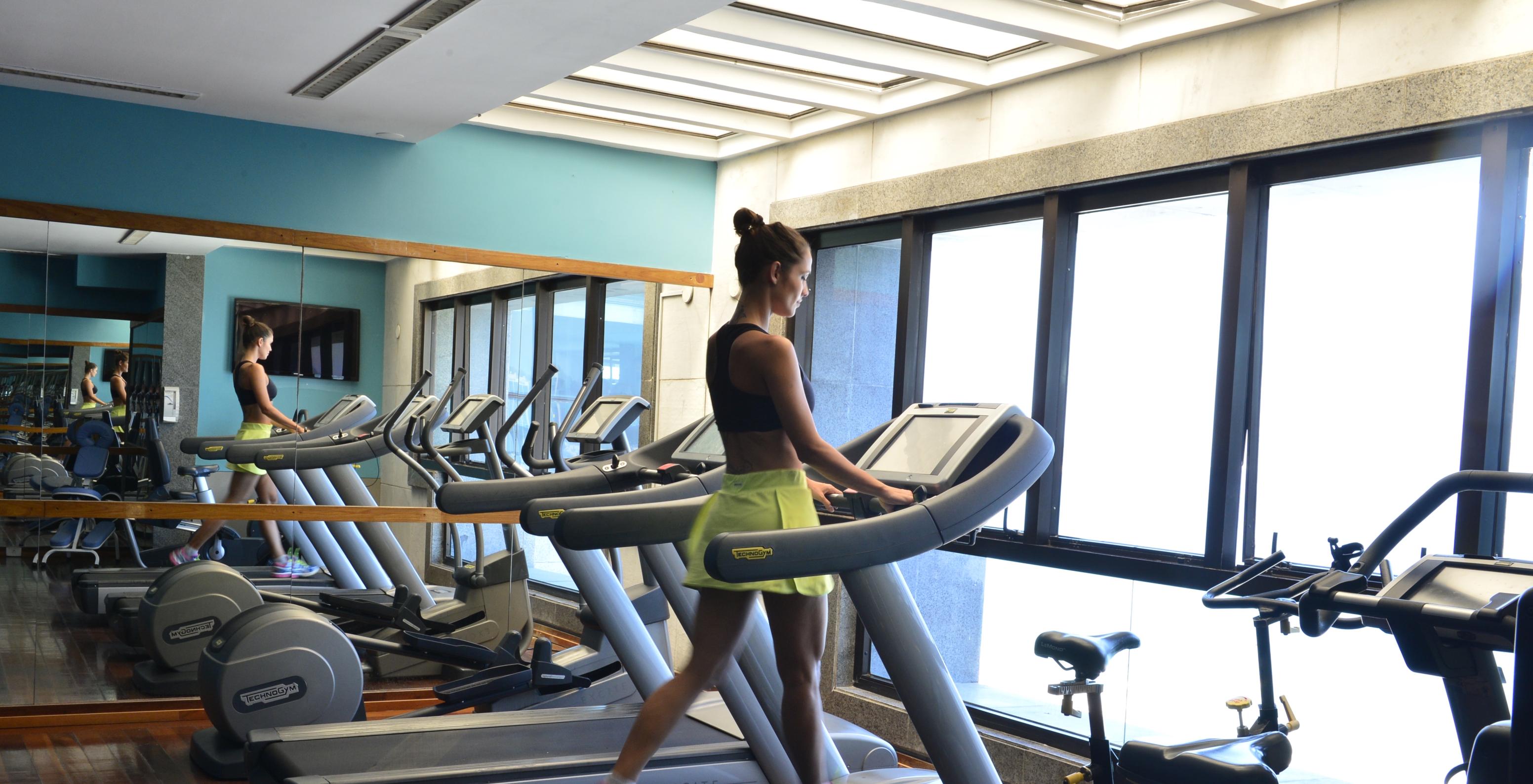 Salle de gym de l'hôtel près de la plage de Copacabana, avec plusieurs machines et miroir et fille s'entraînant sur le tapis