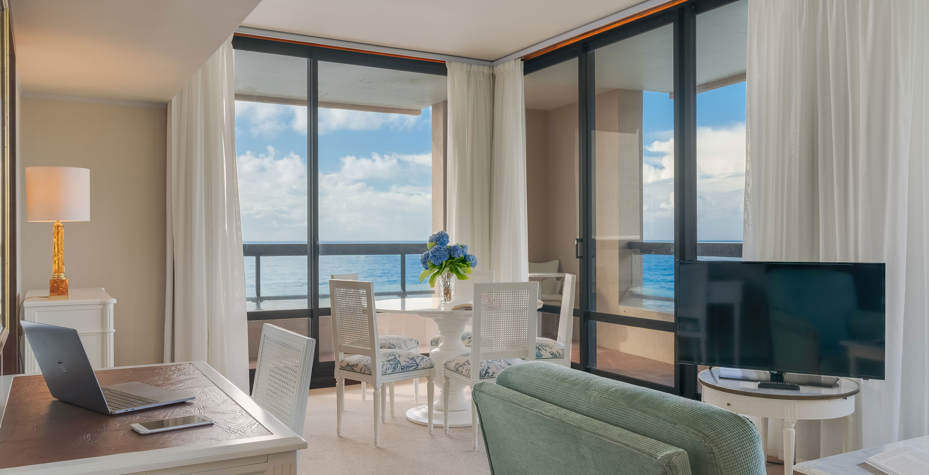 La Suite du Pestana Bahia Praia a un salon avec bureau une table et un canapé avec télévision avec vue sur la mer