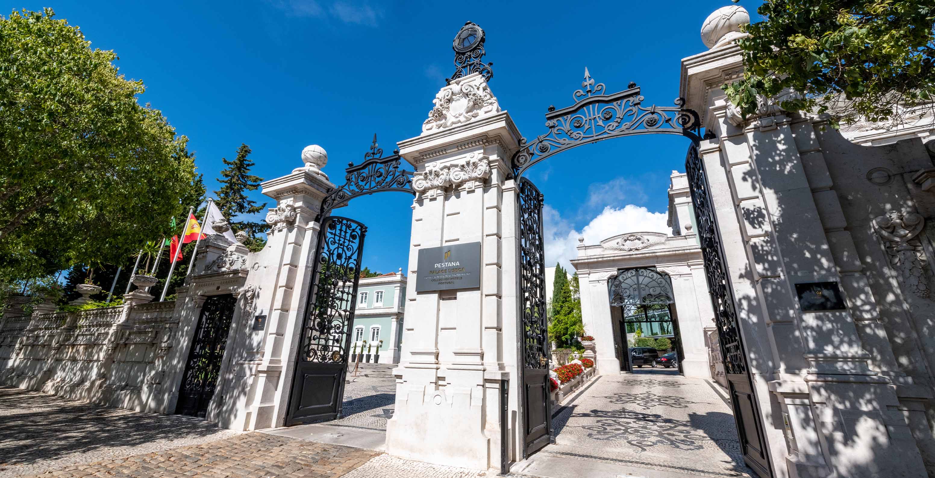 Entrée principale du Pestana Palace Lisbonne, avec deux grands portails, plusieurs drapeaux et pavé portugais au sol