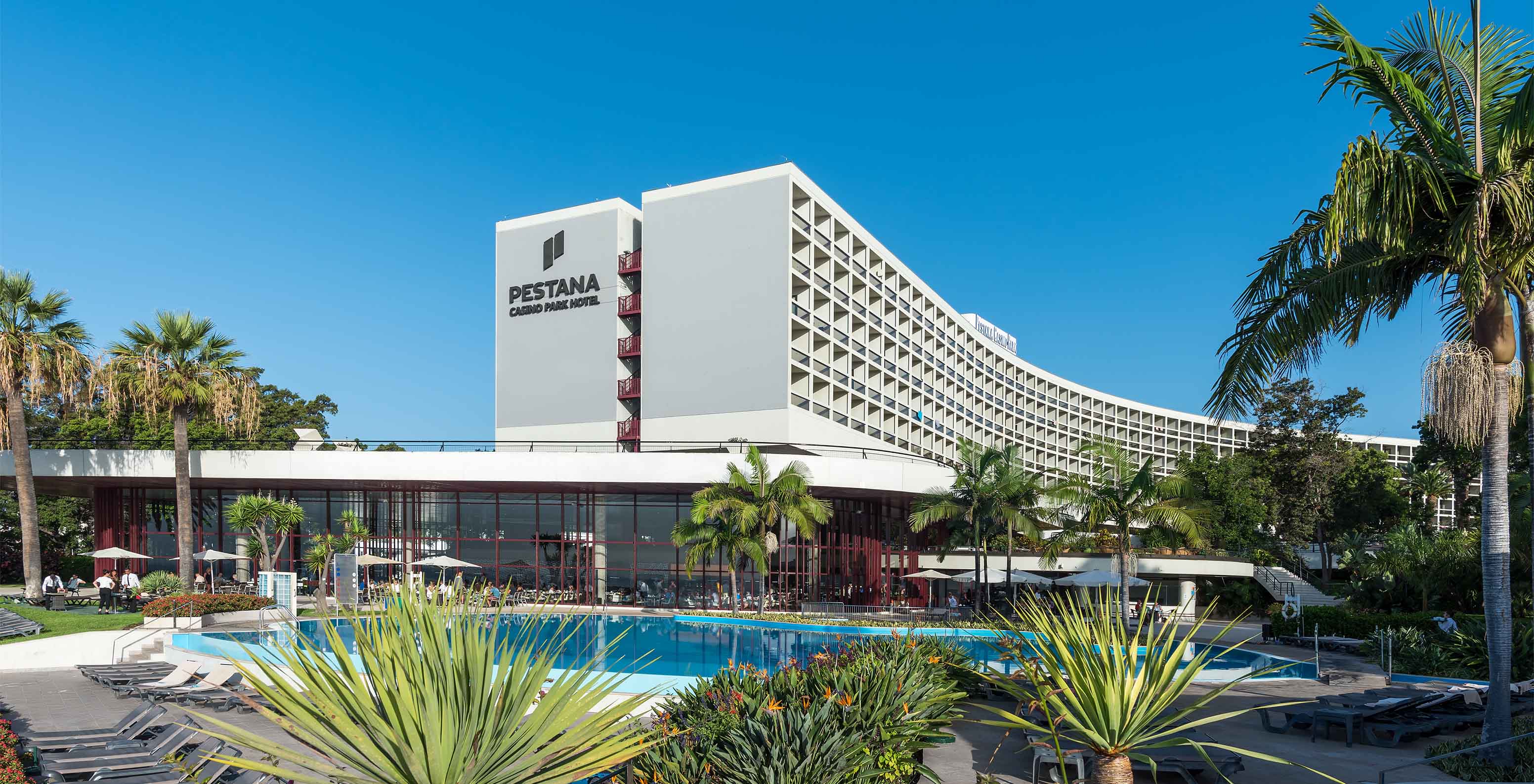 Vue extérieure du Pestana Casino Park, avec piscine et transats entourés de fleurs et de palmiers