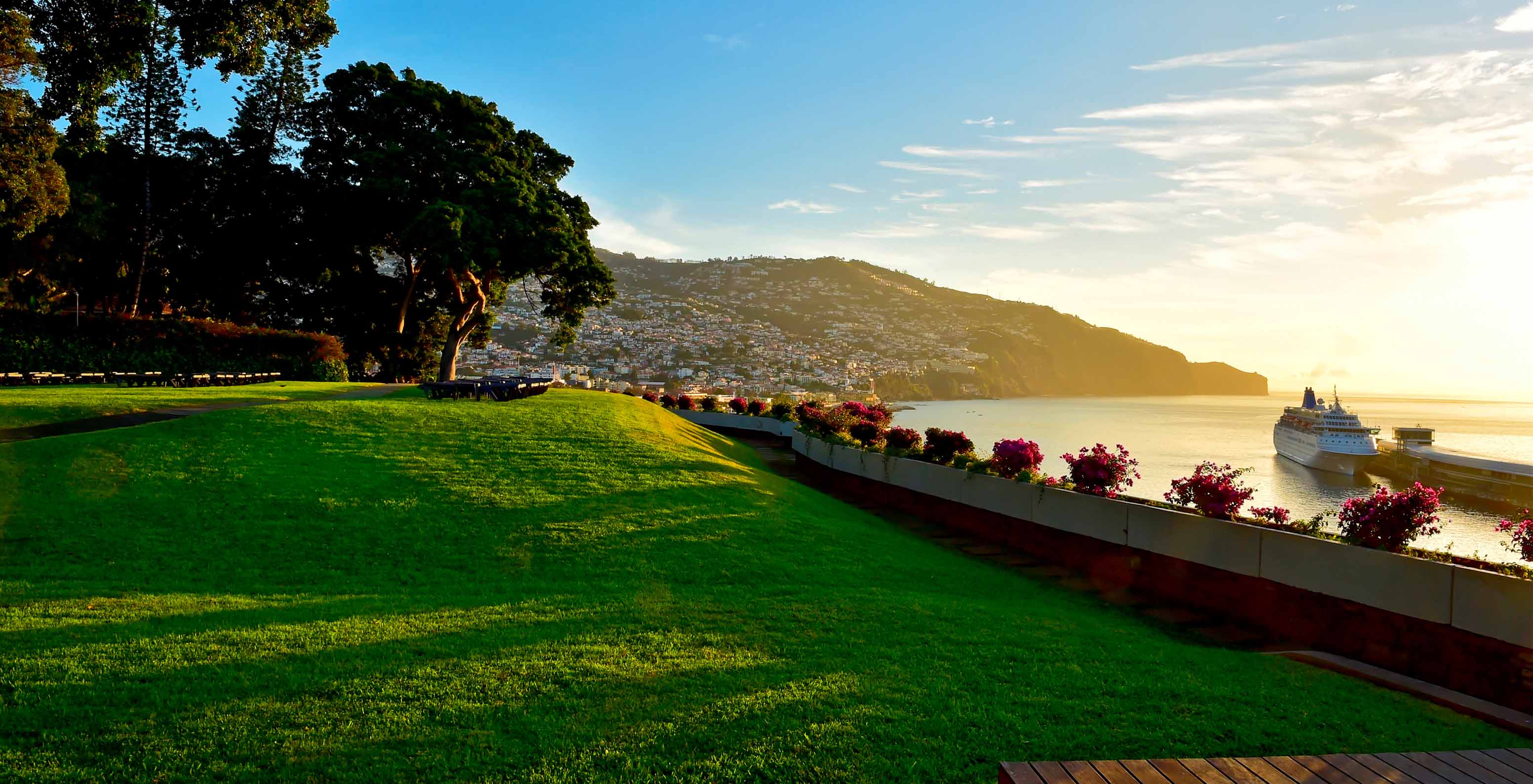 Vue du jardin du Pestana Casino Park au coucher du soleil, avec une ville en arrière-plan et un croiseur ancré