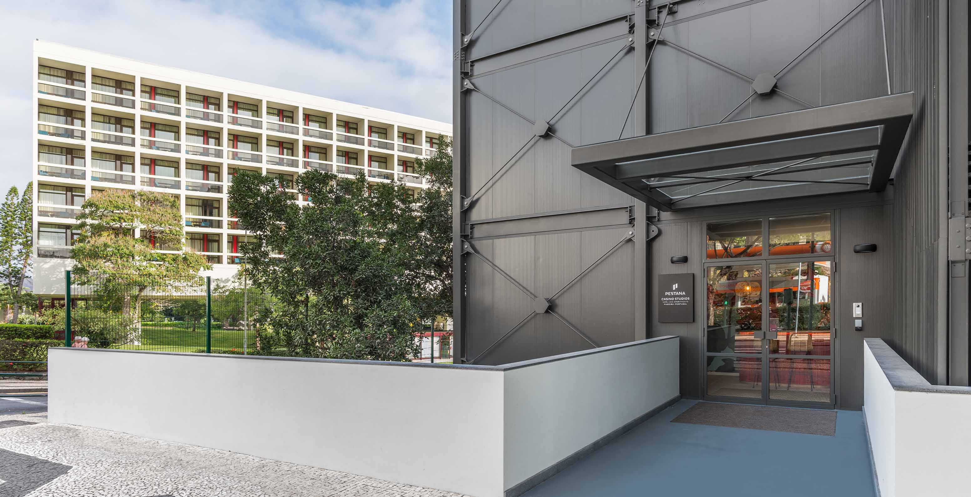 Entrée du Pestana Casino Studios, avec une façade noire, un bâtiment blanc derrière et des arbres