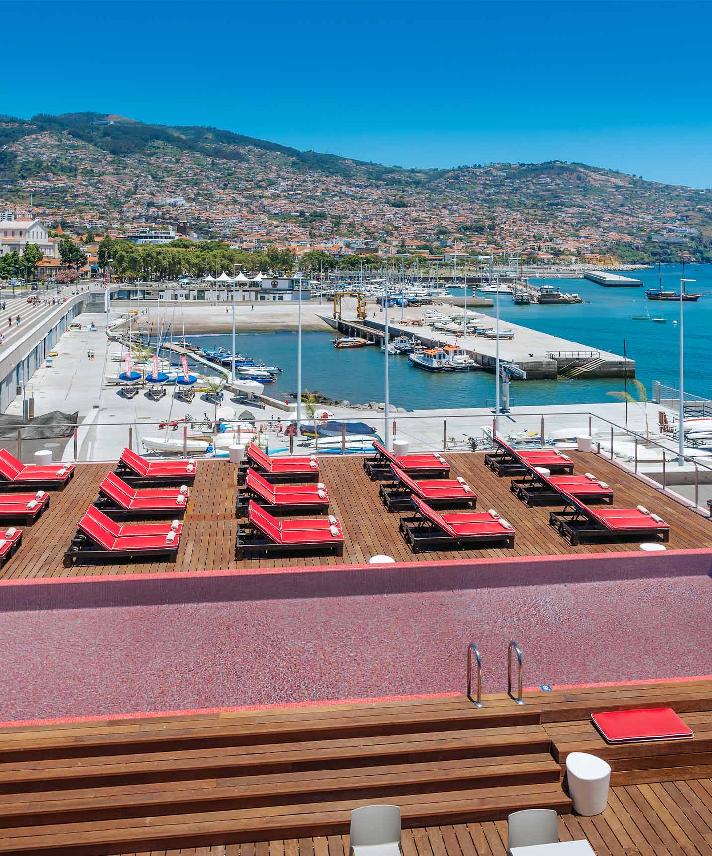 Toit-terrasse du Pestana CR7 Funchal, avec piscine extérieure en rose, plusieurs chaises longues et vue sur Funchal