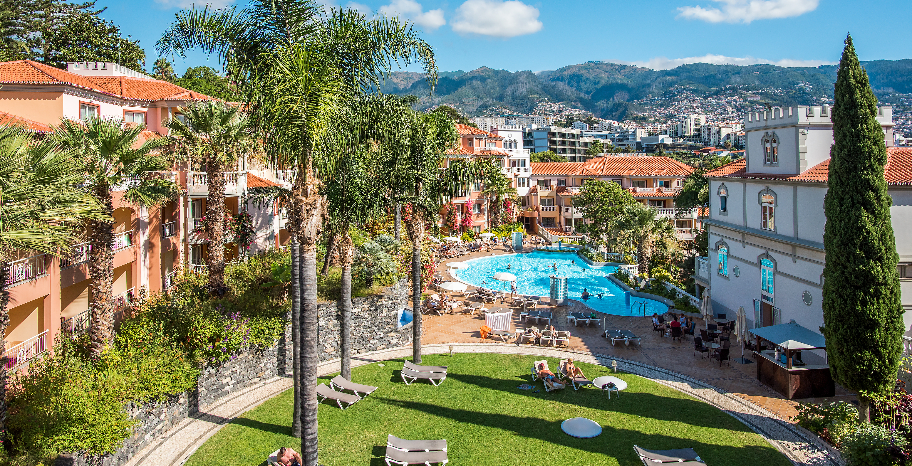 Vue aérienne du Pestana Miramar, avec des gens dans la piscine et des chaises longues, entouré par la nature et bâtiments