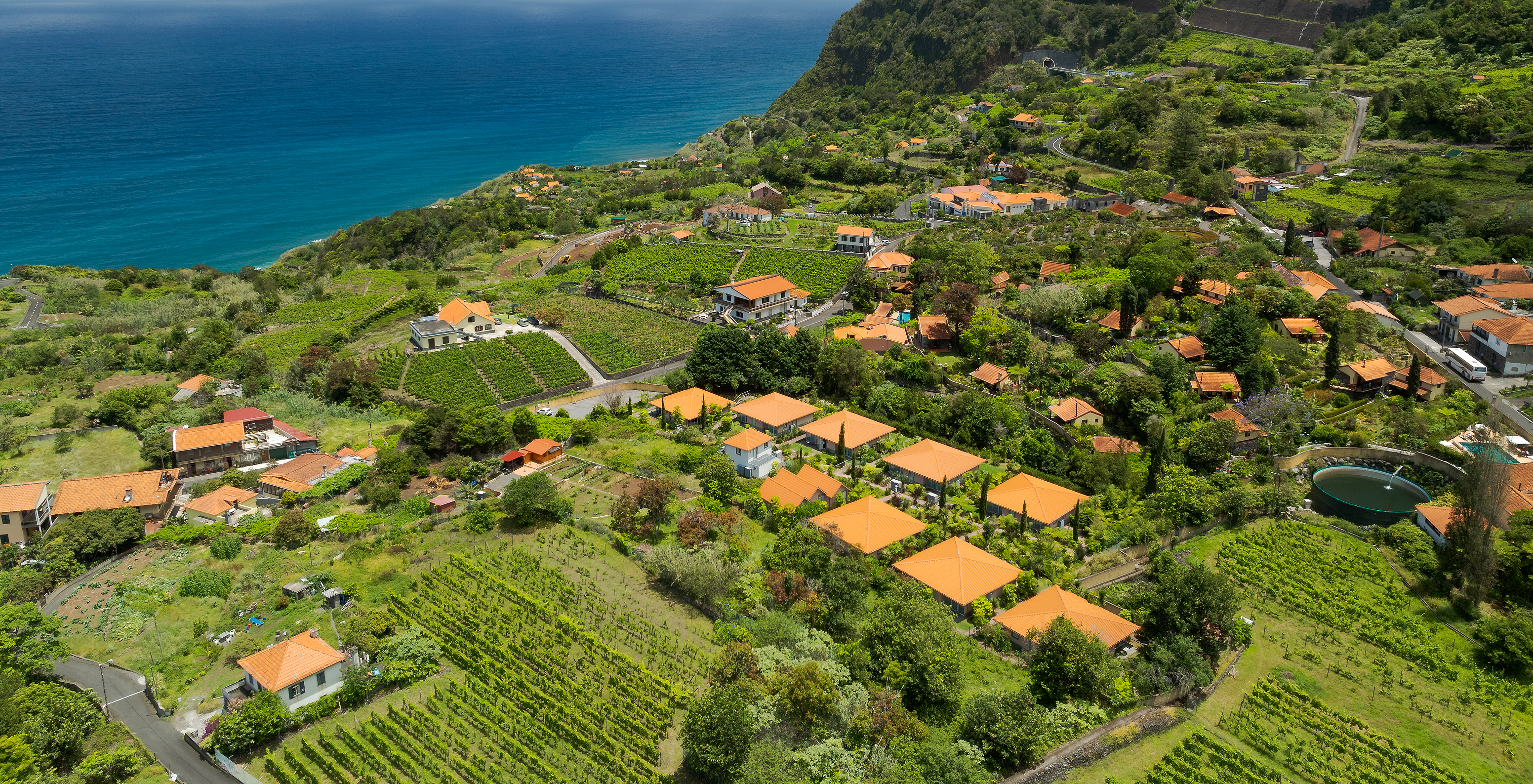 Vue aérienne du Pestana Quinta do Arco, avec les montagnes et champs verts autour, avec l'océan en arrière-plan