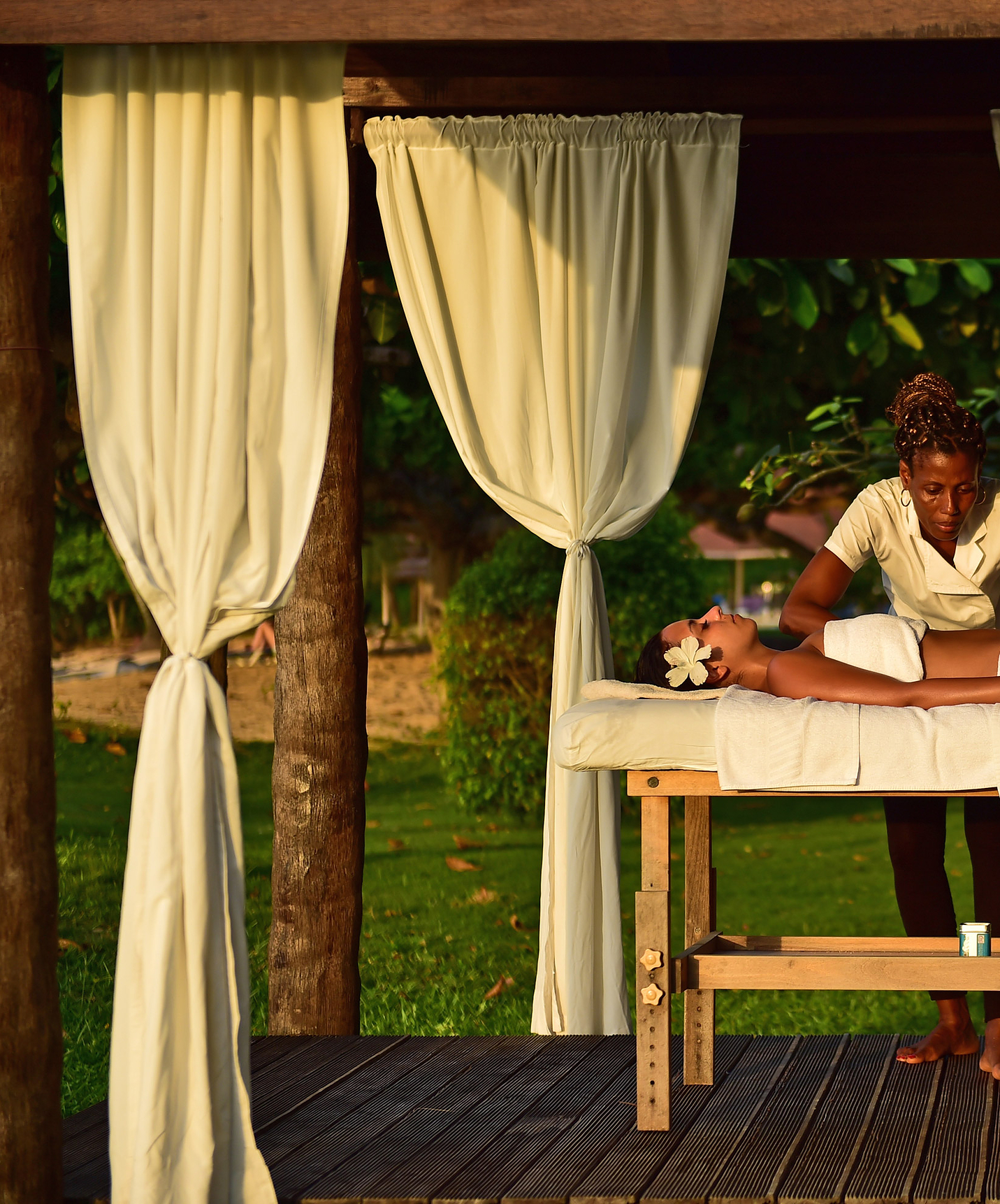 Fille avec une fleur dans les cheveux reçoit un massage en plein air à l'hôtel de vacances avec piscine, face à la plage