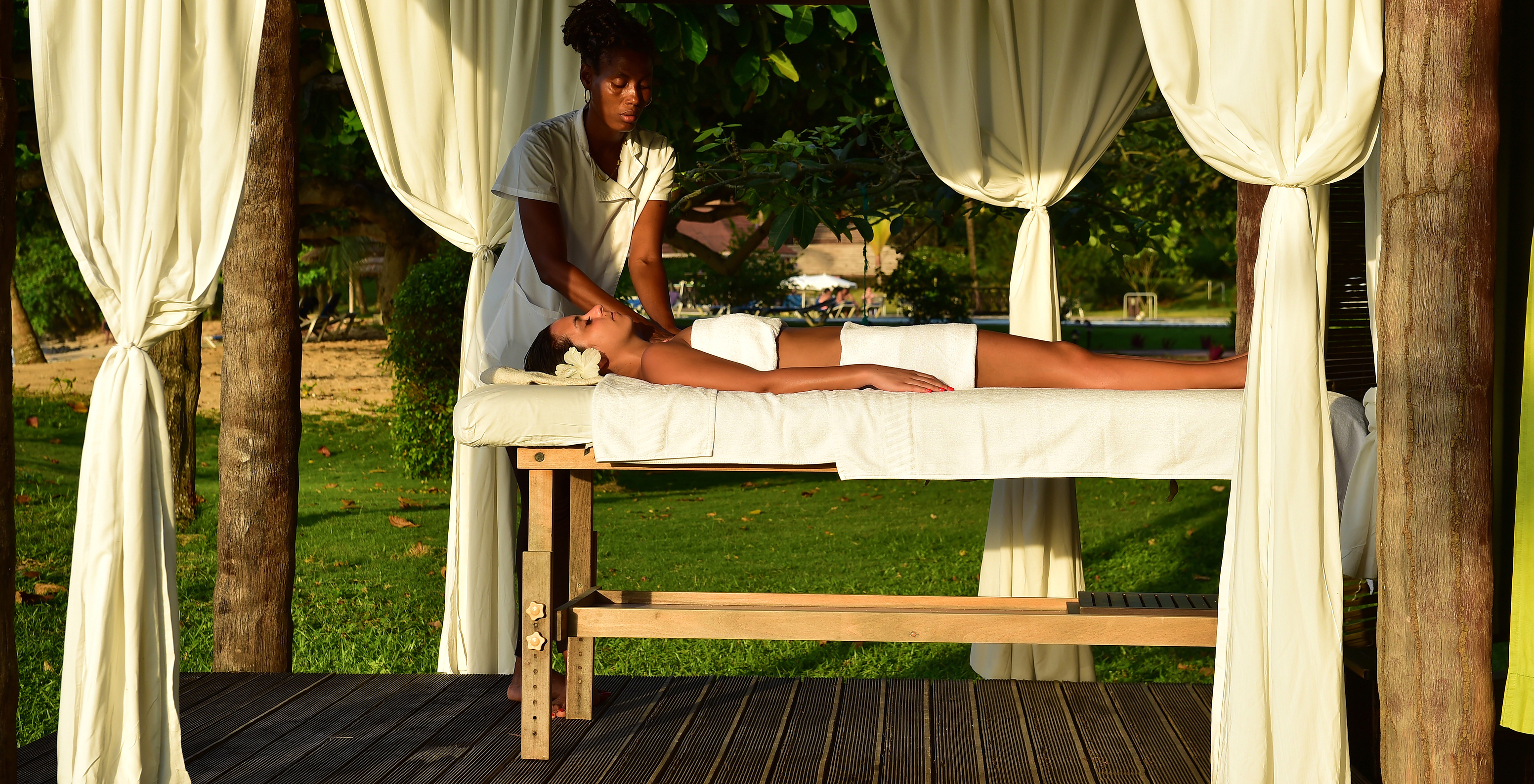 Fille avec une fleur dans les cheveux recevant un massage en plein air à l'hôtel pour vacances, avec piscine et spa