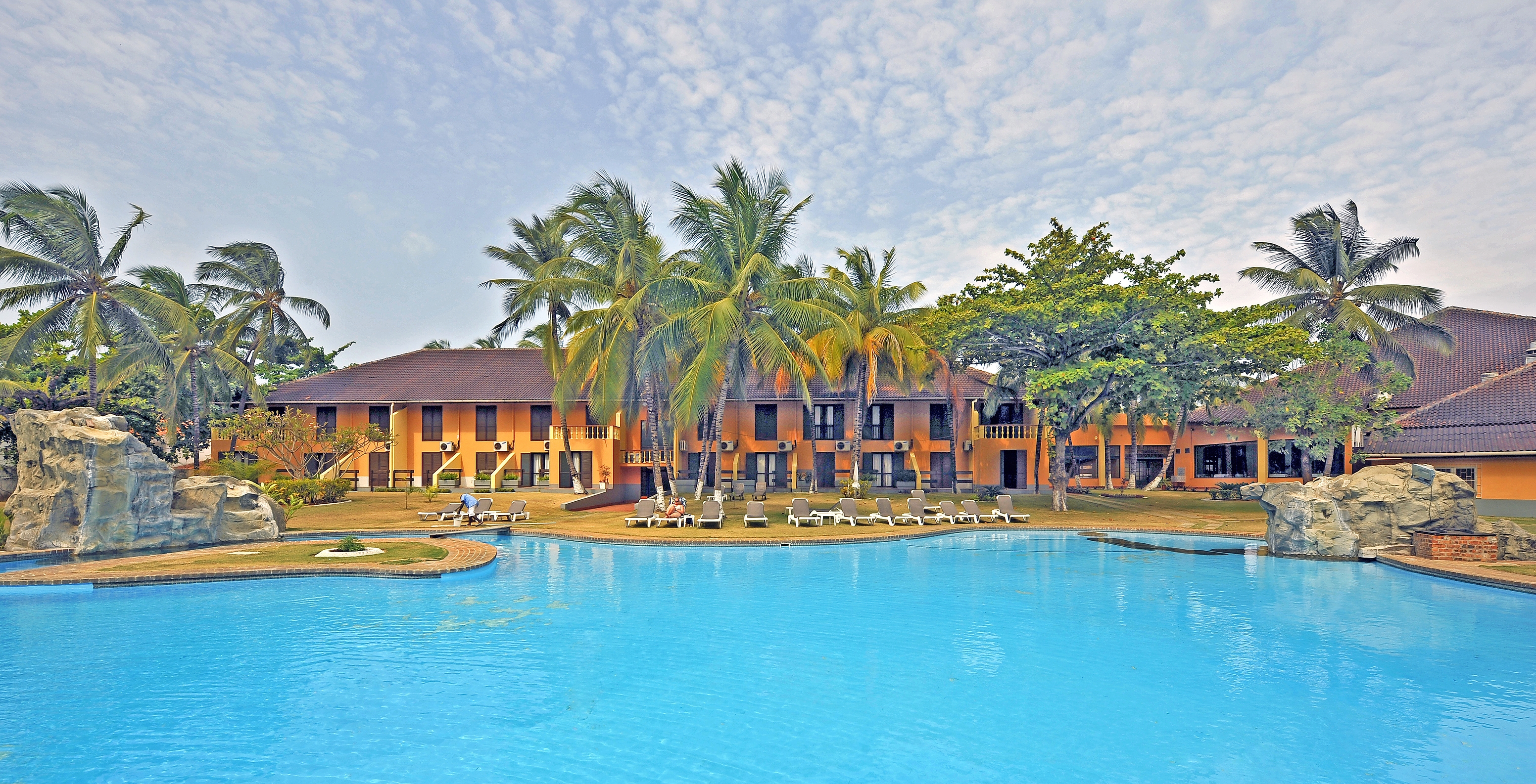 Façade du bâtiment jaune du Pestana Miramar São Tomé, avec la piscine extérieure devant et plusieurs chaises longues