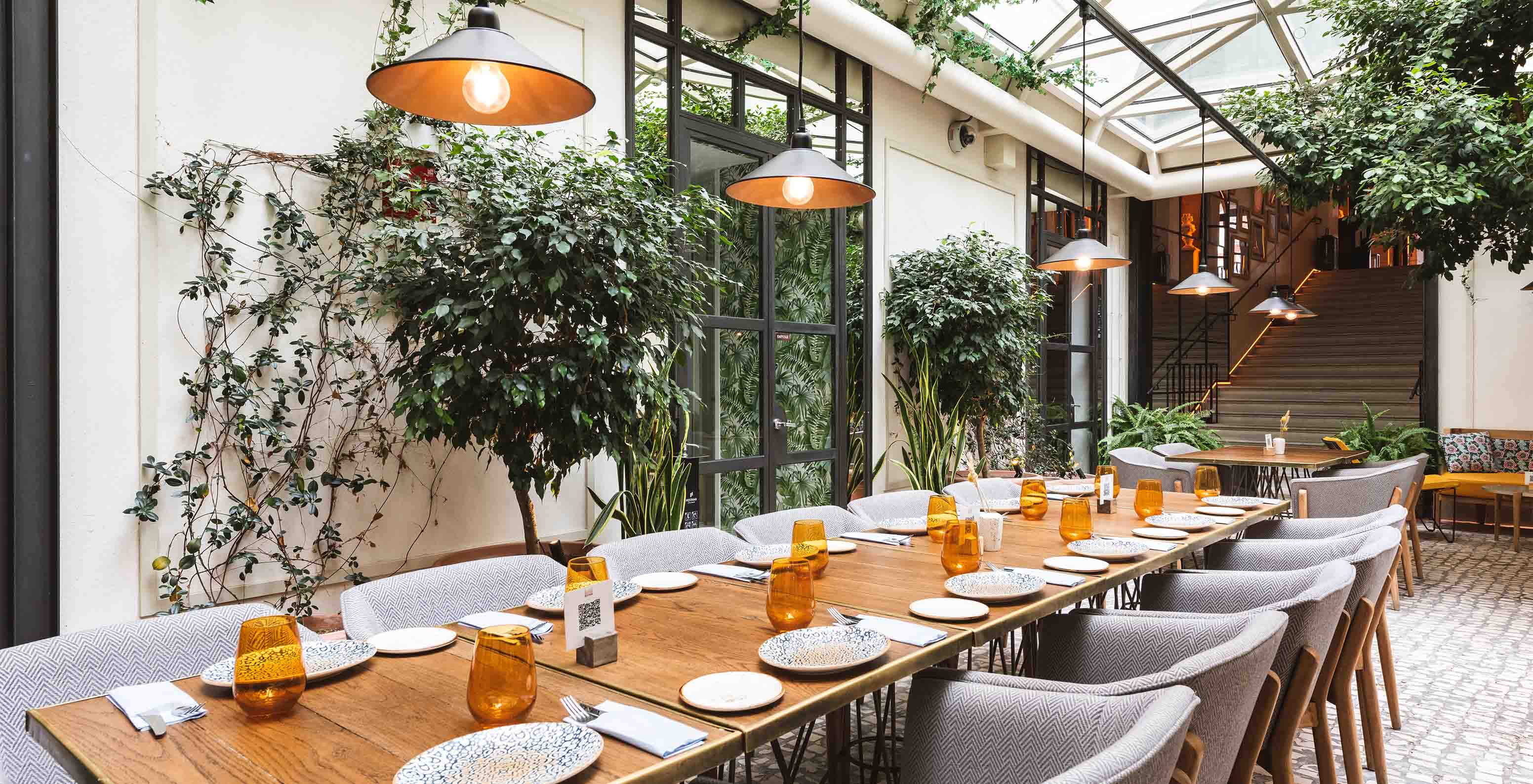 Table pour repas au restaurant de l'hôtel avec végétation au plafond et lumière naturelle