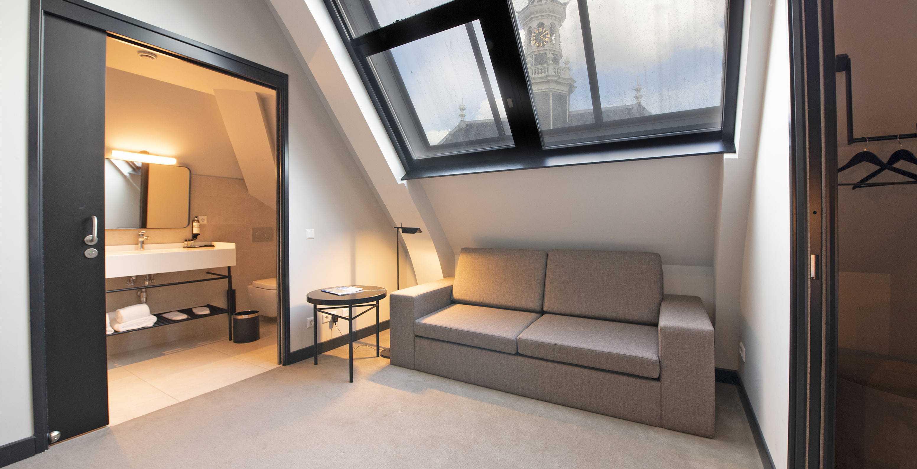 La chambre Loft du Pestana Amsterdam Riverside a un canapé gris, et une salle de bain avec lavabo et miroir