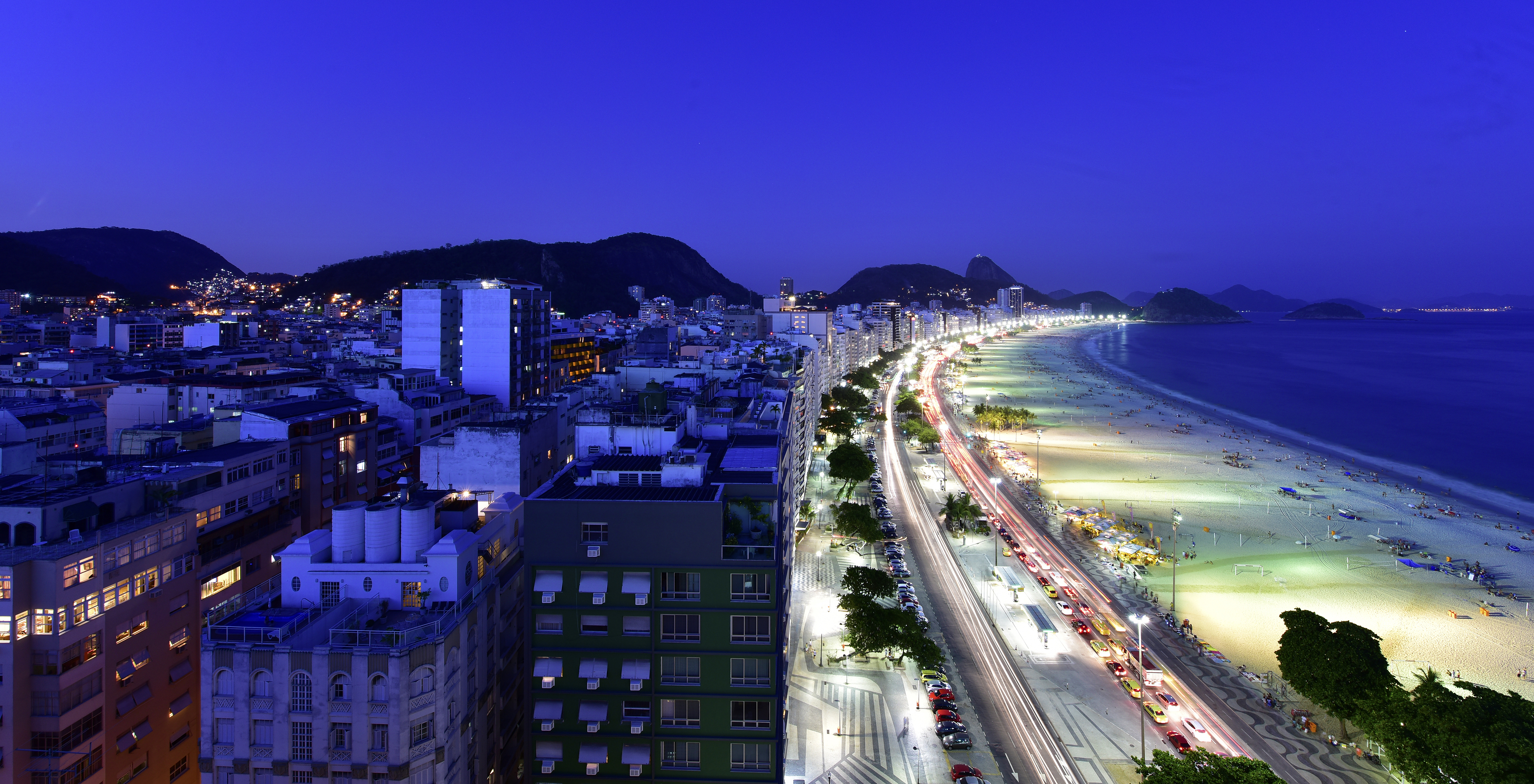 Nachtzicht op het strand van Copacabana, met verlicht zand, donkerblauwe zee en hemel en bergen op de achtergrond