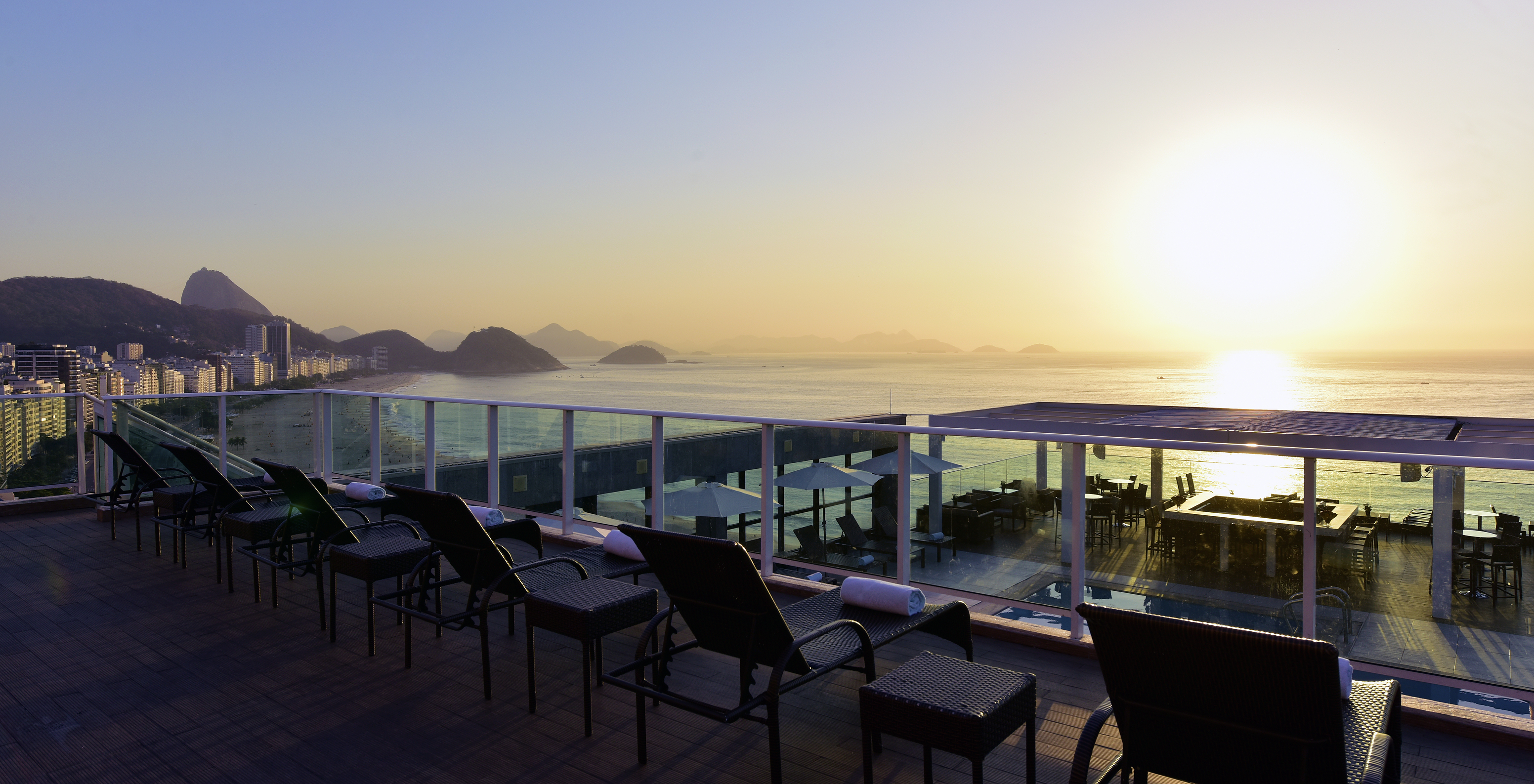 Rooftop van het hotel naast Copacabana strand, met ligstoelen en uitzicht op zee en bergen tijdens zonsondergang