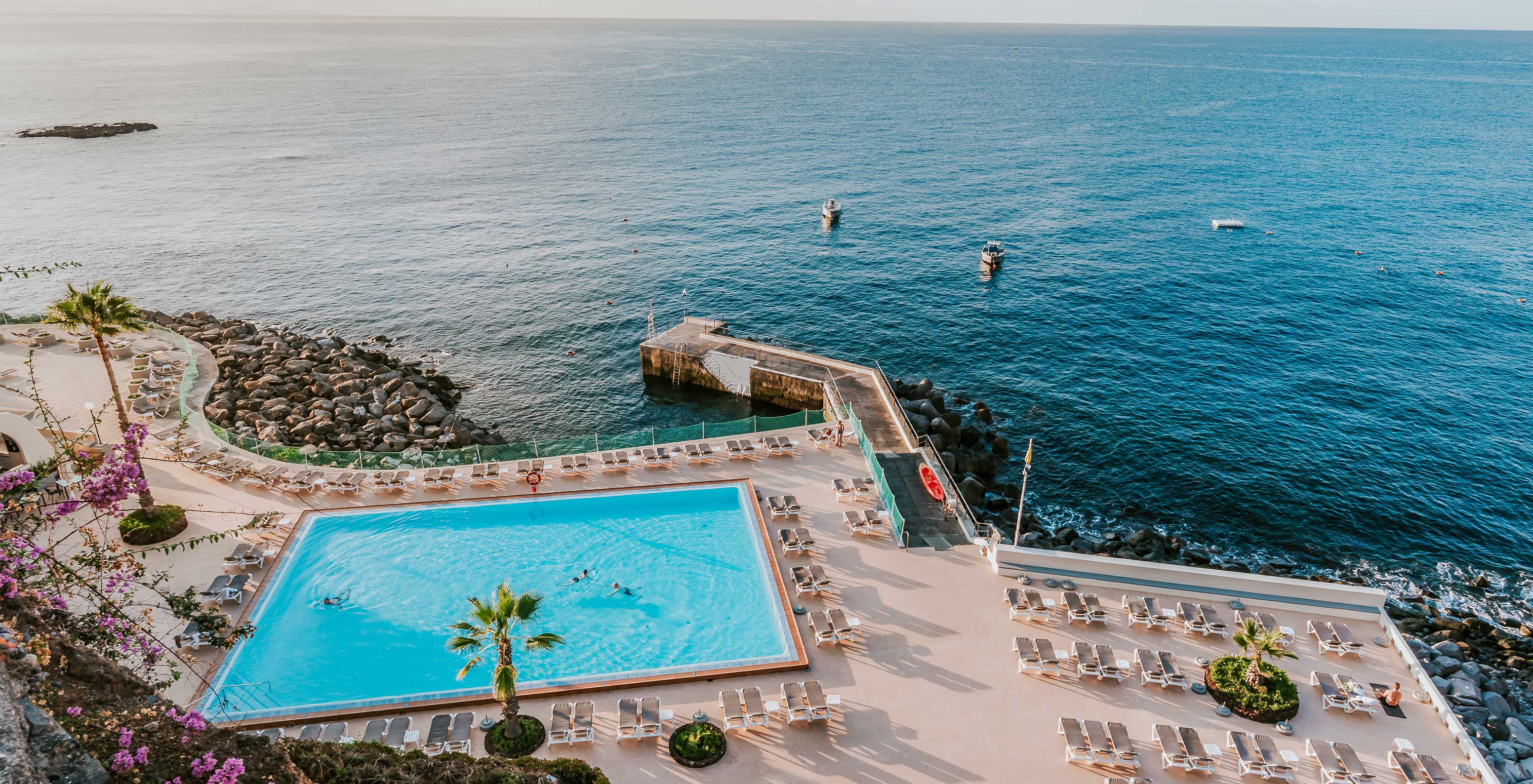 Luchtfoto van het zwembad van Pestana Carlton Madeira, met ligstoelen en uitzicht op de Atlantische Oceaan