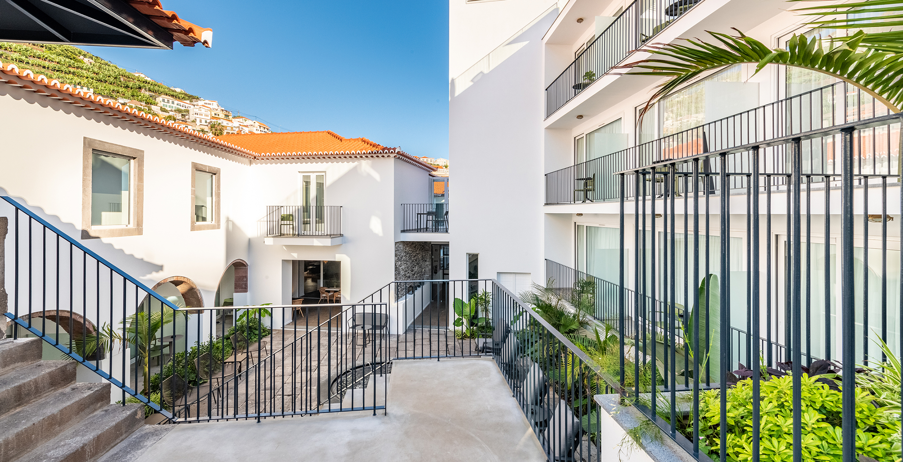 Gevel van de binnenplaats van een hotel in Câmara de Lobos, Madeira, met veel planten, balkons en een terras