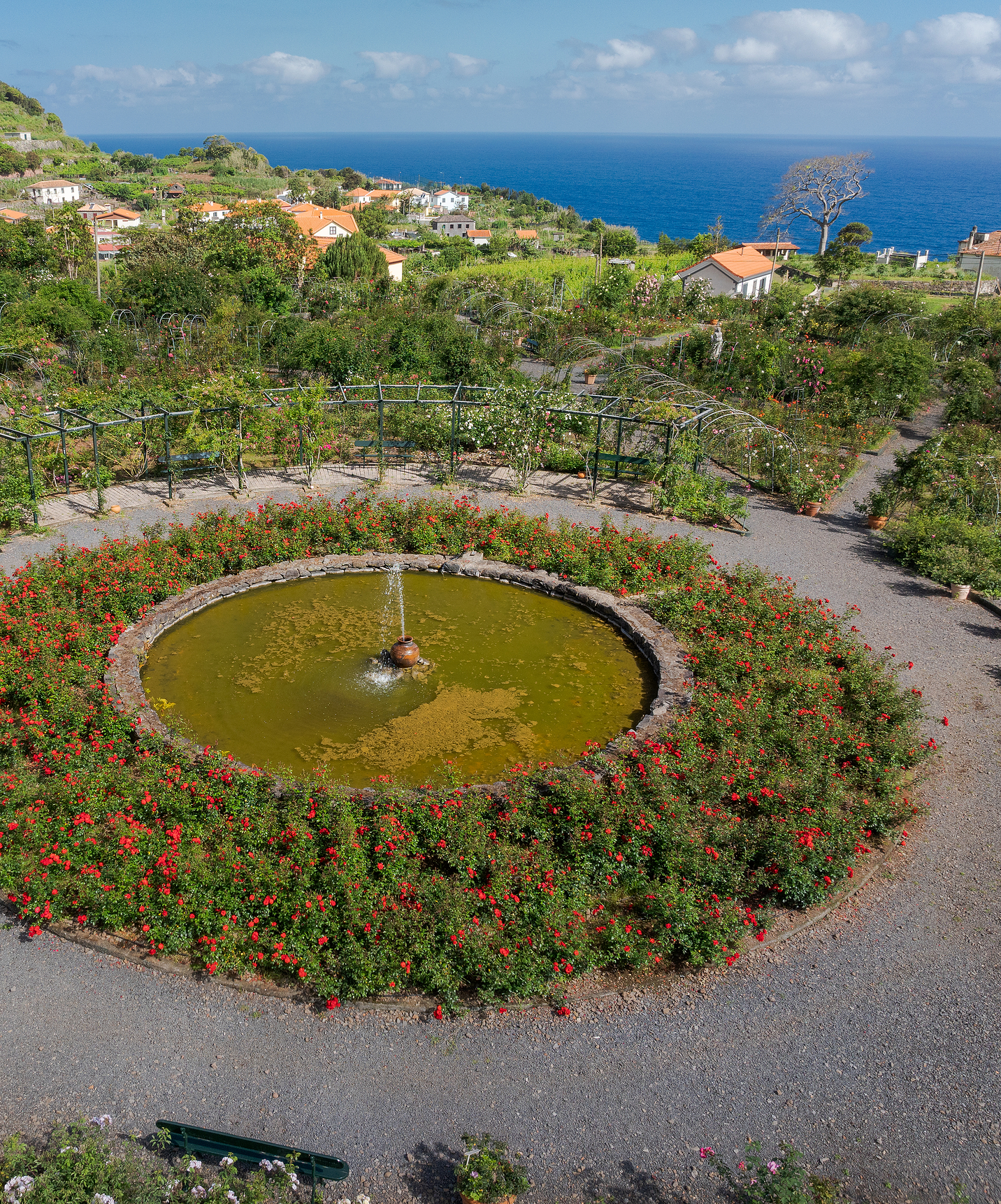 Uitzicht van boven op rozentuin van Quinta do Arco met fontein in het midden omgeven door bloemen en zeezicht