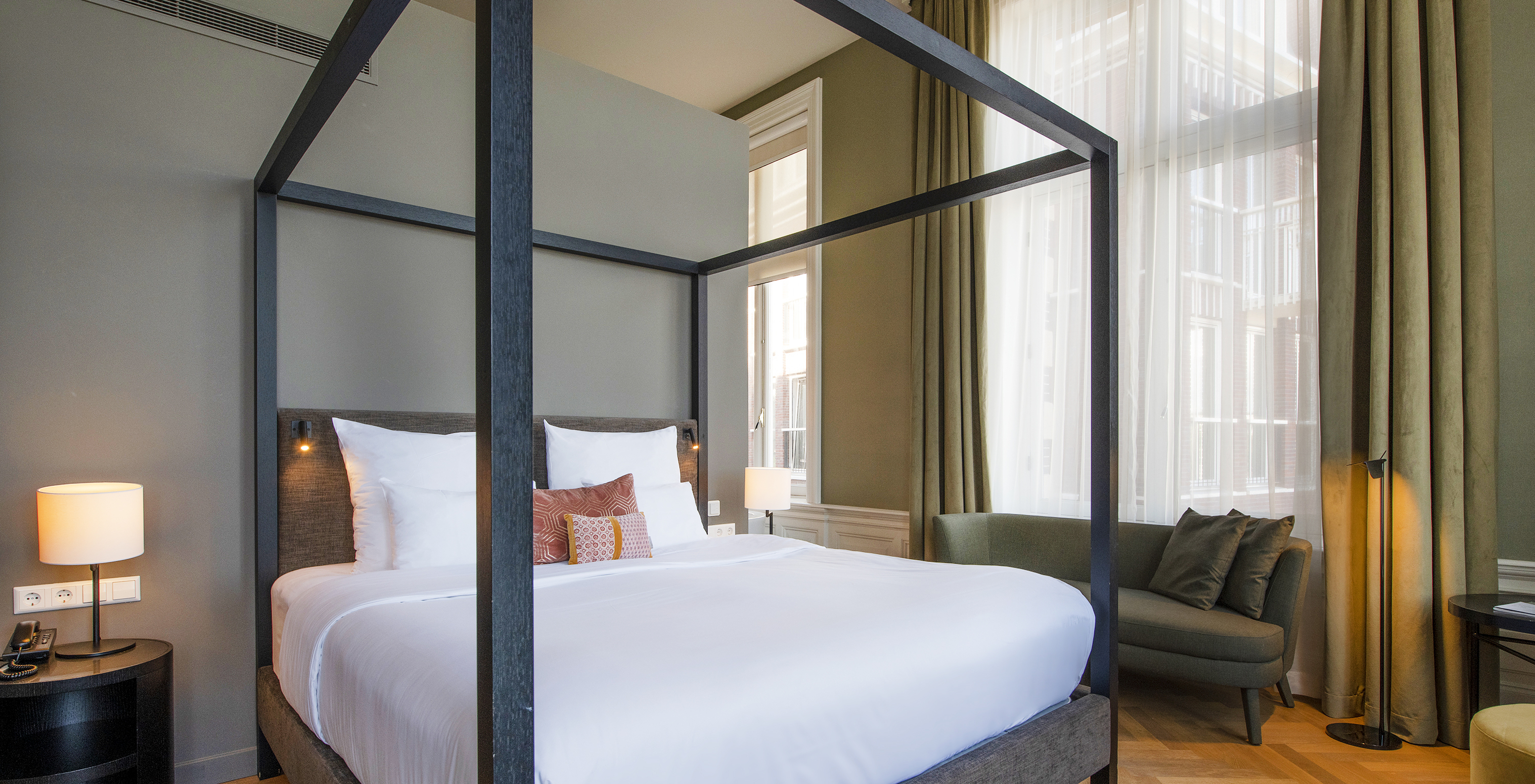 Junior Suite - River View van Pestana Amsterdam Riverside heeft tweepersoonsbed met hemelbed en groene bank