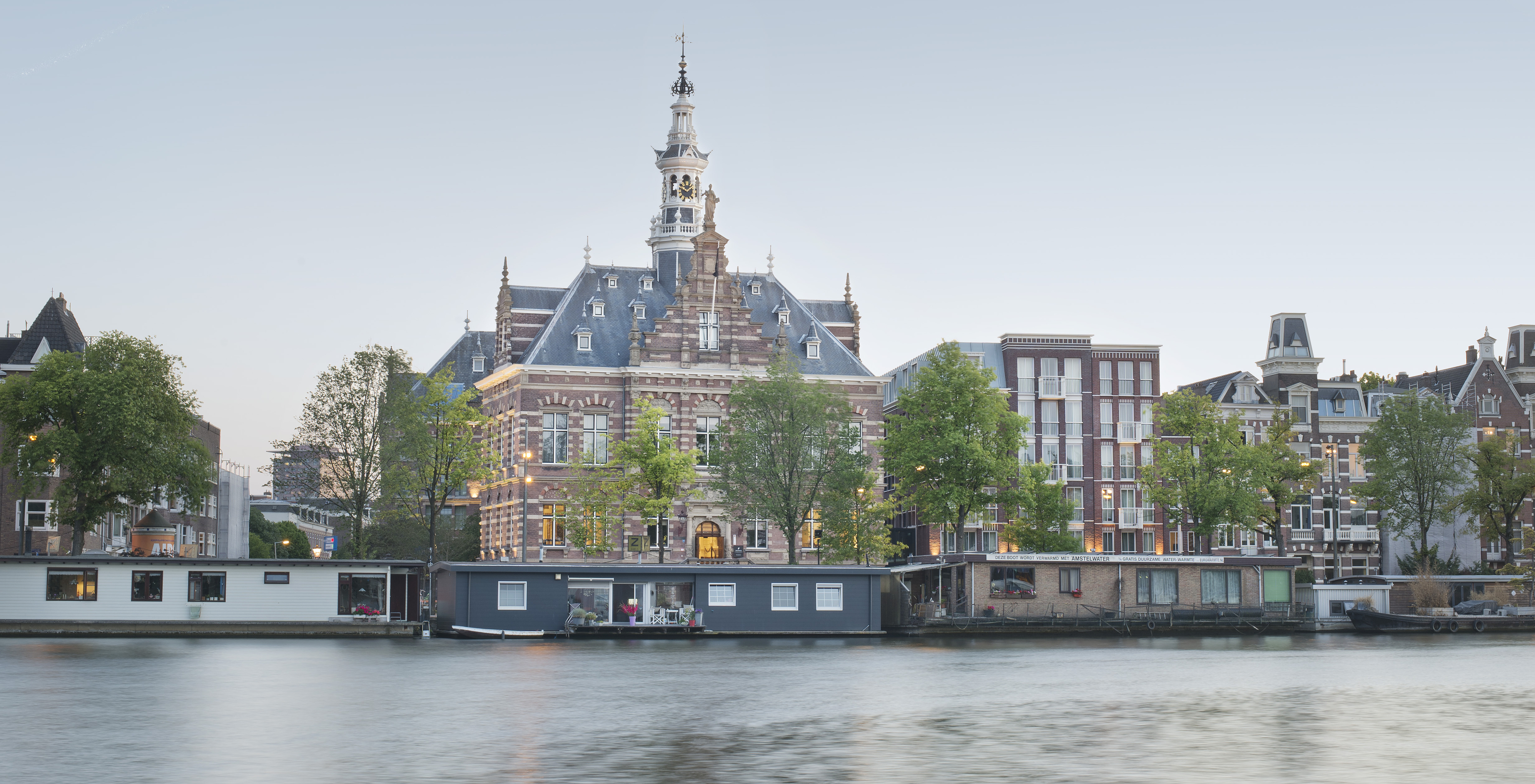 Panoramisch uitzicht op Pestana Amsterdam Riverside bij schemering, vanaf het kanaal omringd door typische huizen