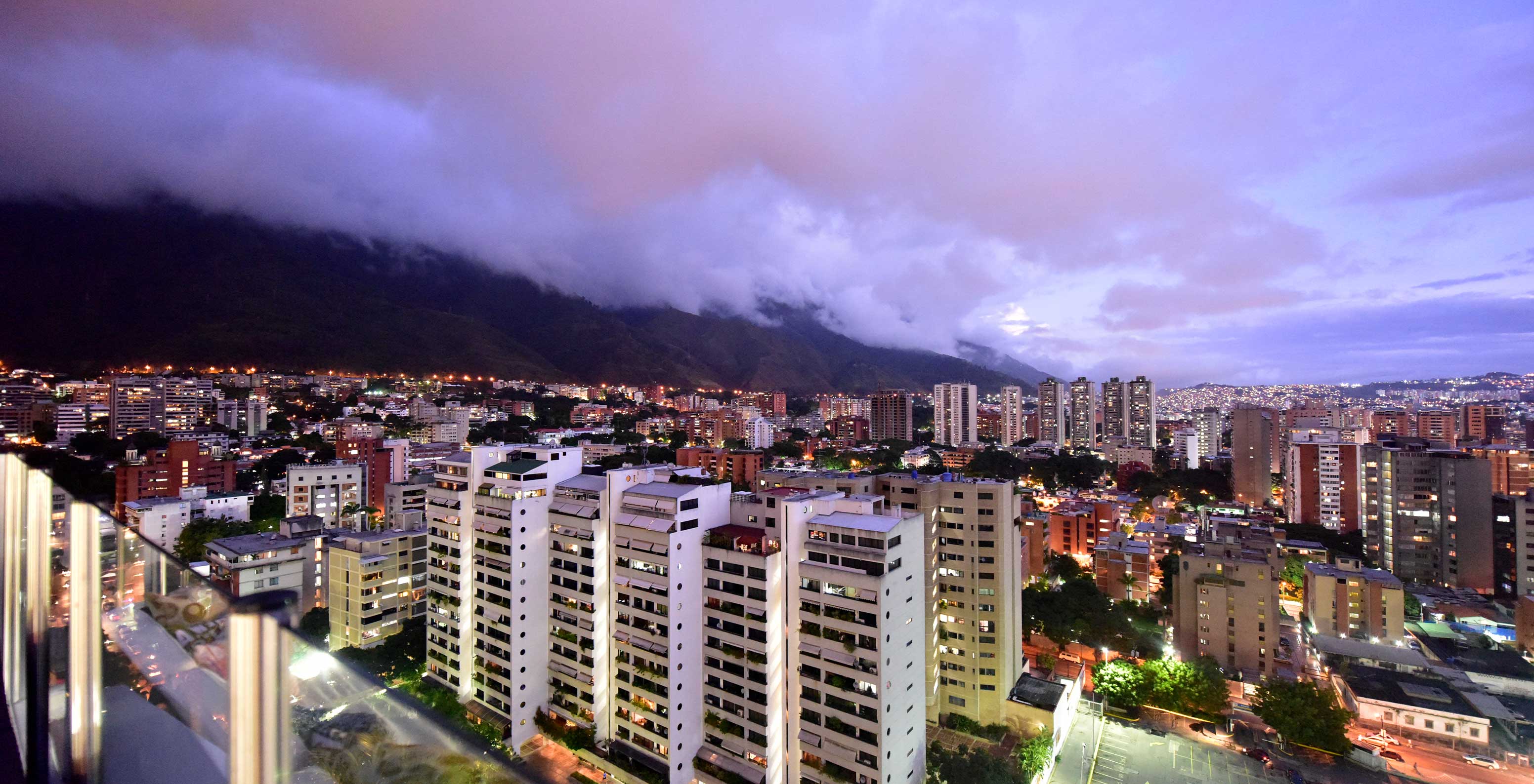 Nachtelijk uitzicht op Pestana Caracas, met hoge gebouwen en bergen op de achtergrond, nabij het hotel in Caracas