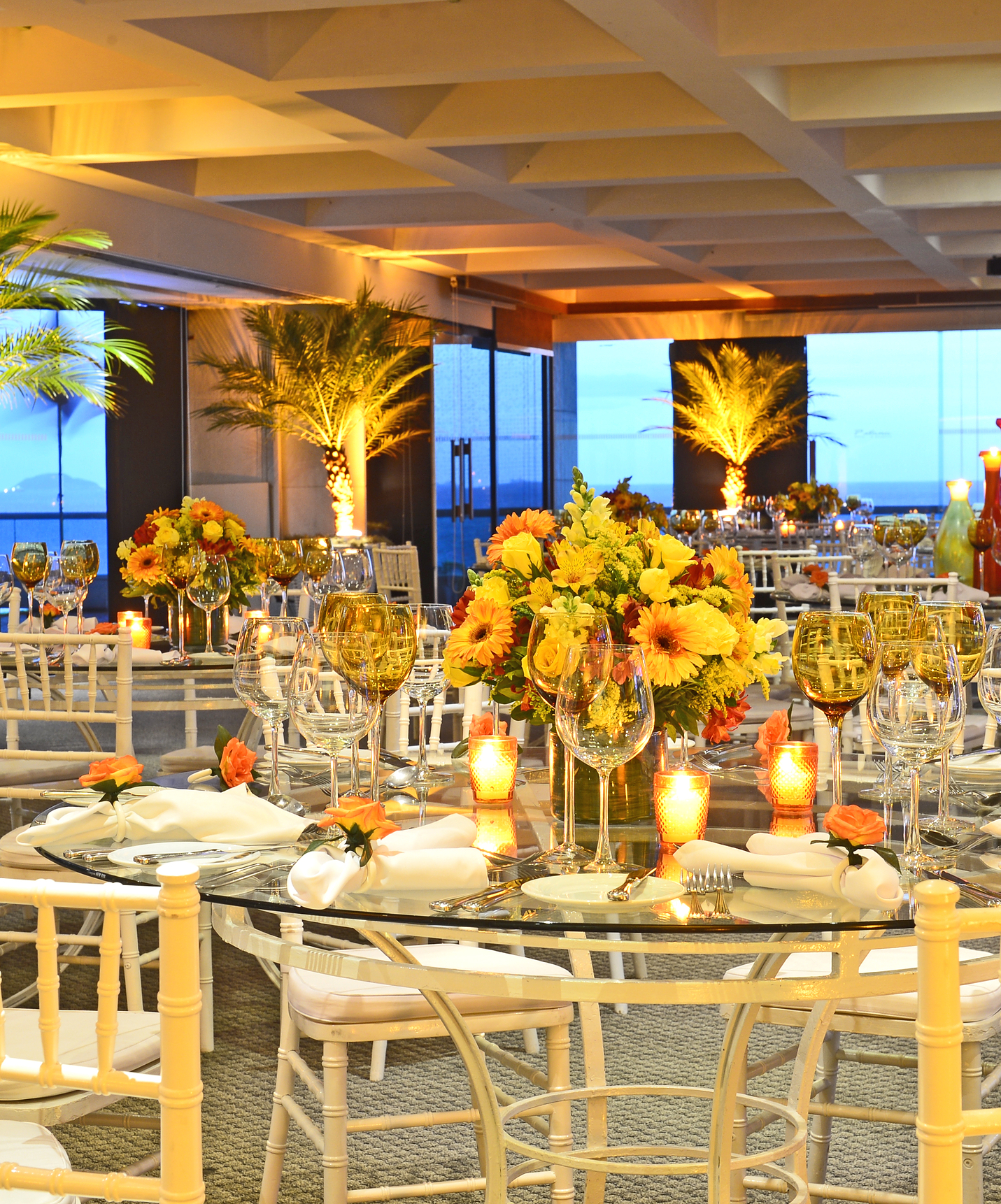 Sala de eventos do Hotel Junto à Praia de Copacabana, com palmeiras iluminadas e várias mesas com centros de flores