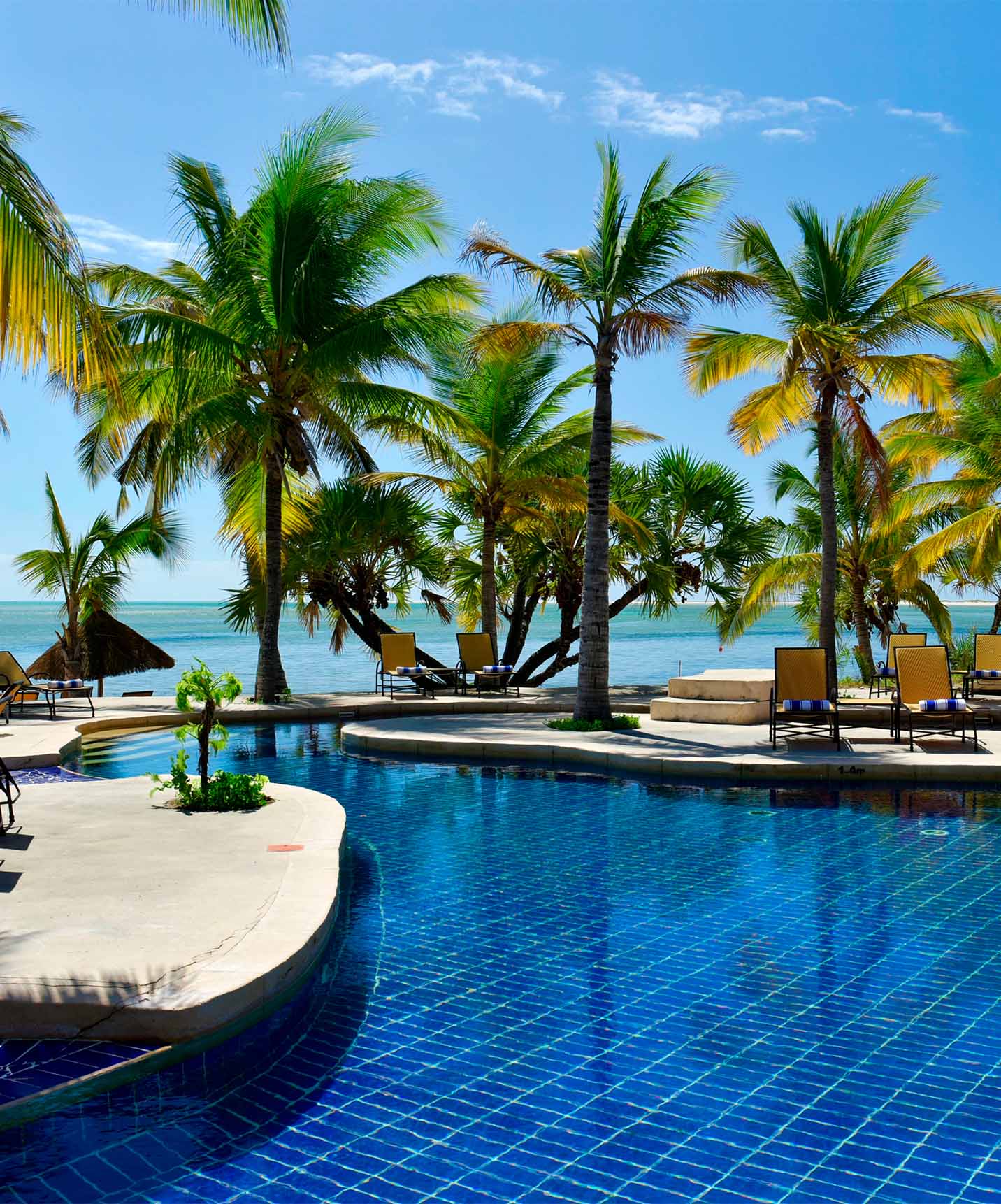 Piscina do Pestana Bazaruto Lodge com espreguiçadeiras à sombra da palmeiras, com a praia em frente