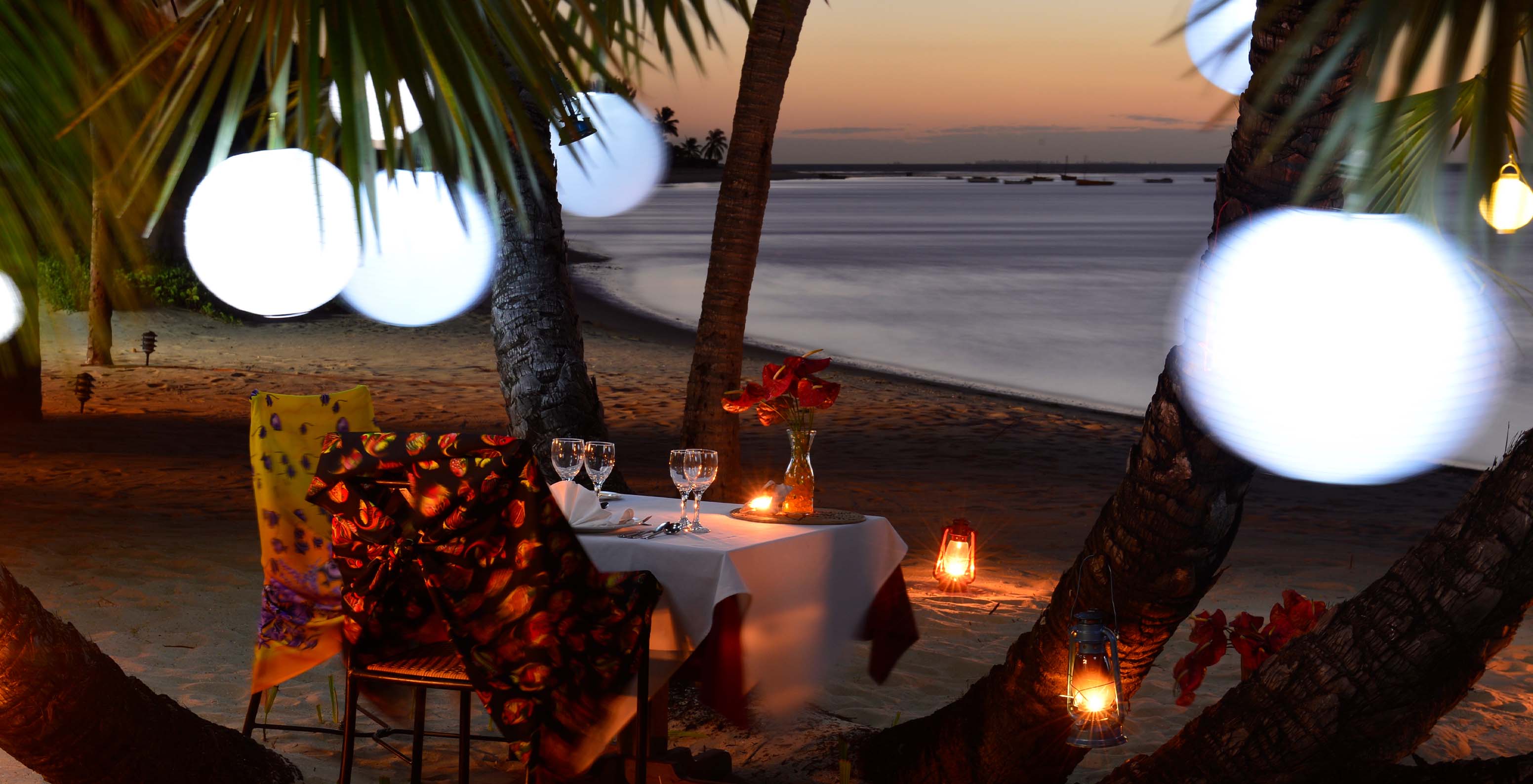 Jantar romântico no meio da praia entre palmeiras e luzes decorativas, o ambiente perfeito para namorar e descansar