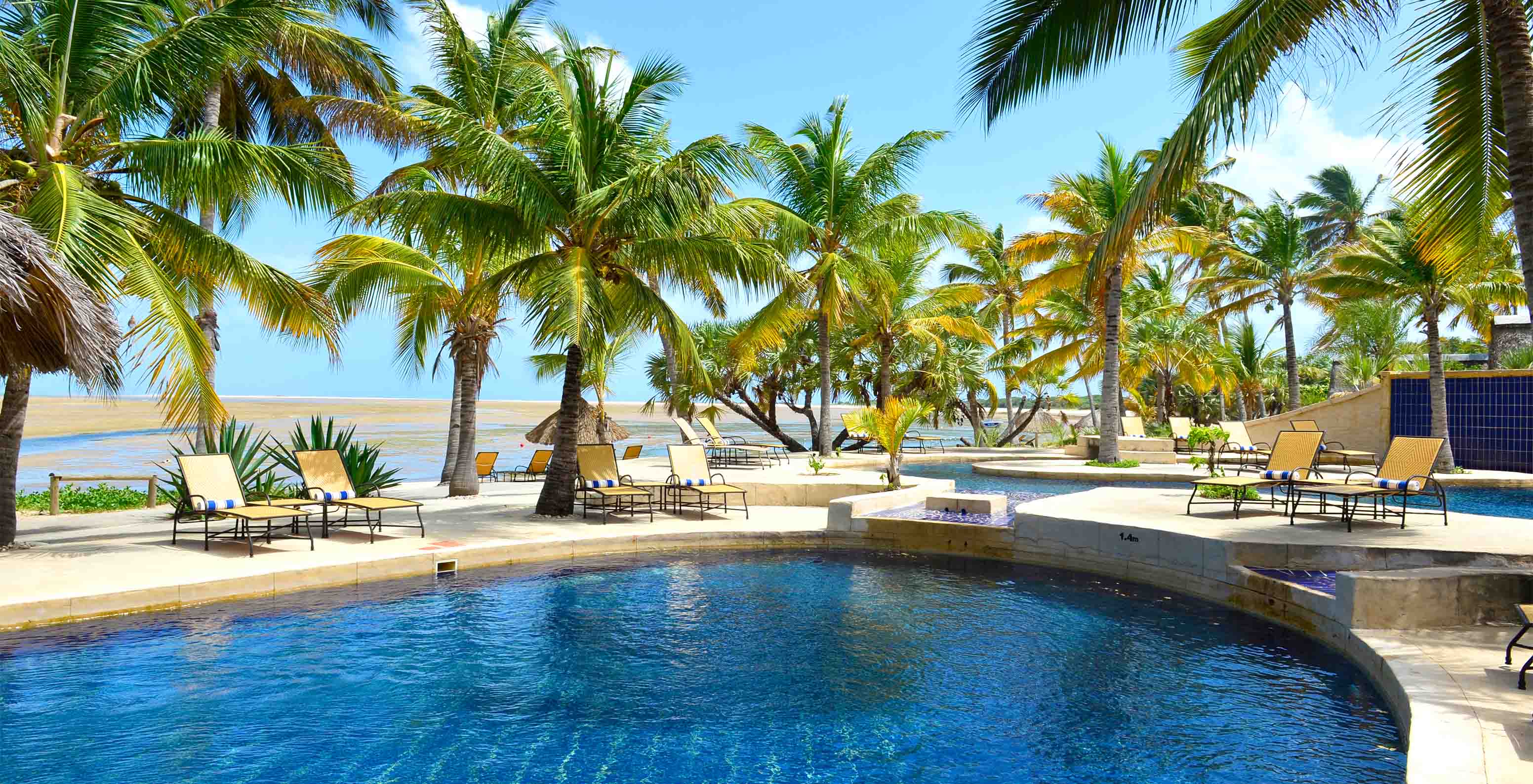 Piscina do Pestana Bazaruto Lodge com espreguiçadeiras à sombra das palmeiras, com a praia em frente