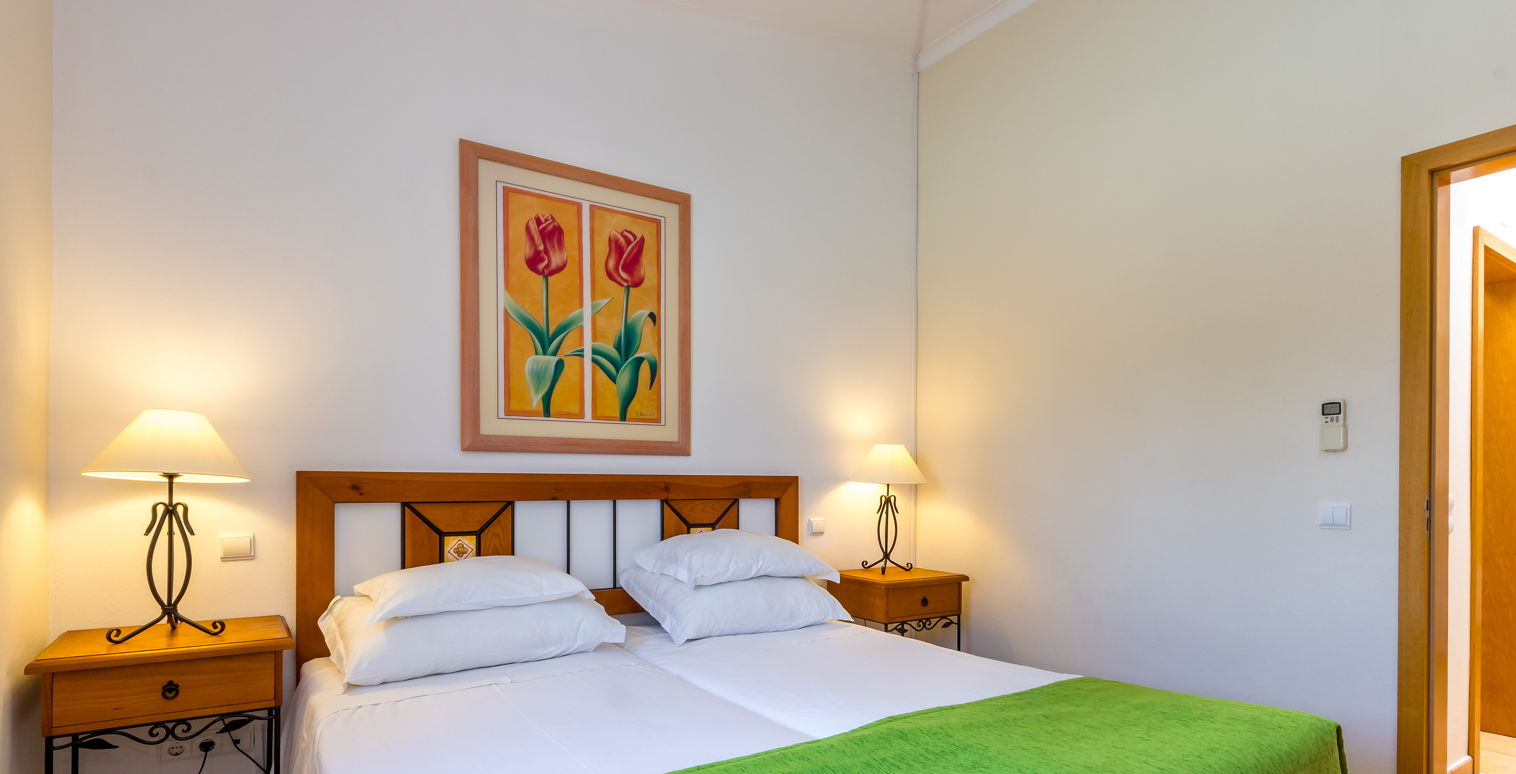 O Apartamento T1 - Terra do Pestana Palm Gardens tem duas camas juntas, com colcha verde e um quadro com duas flores