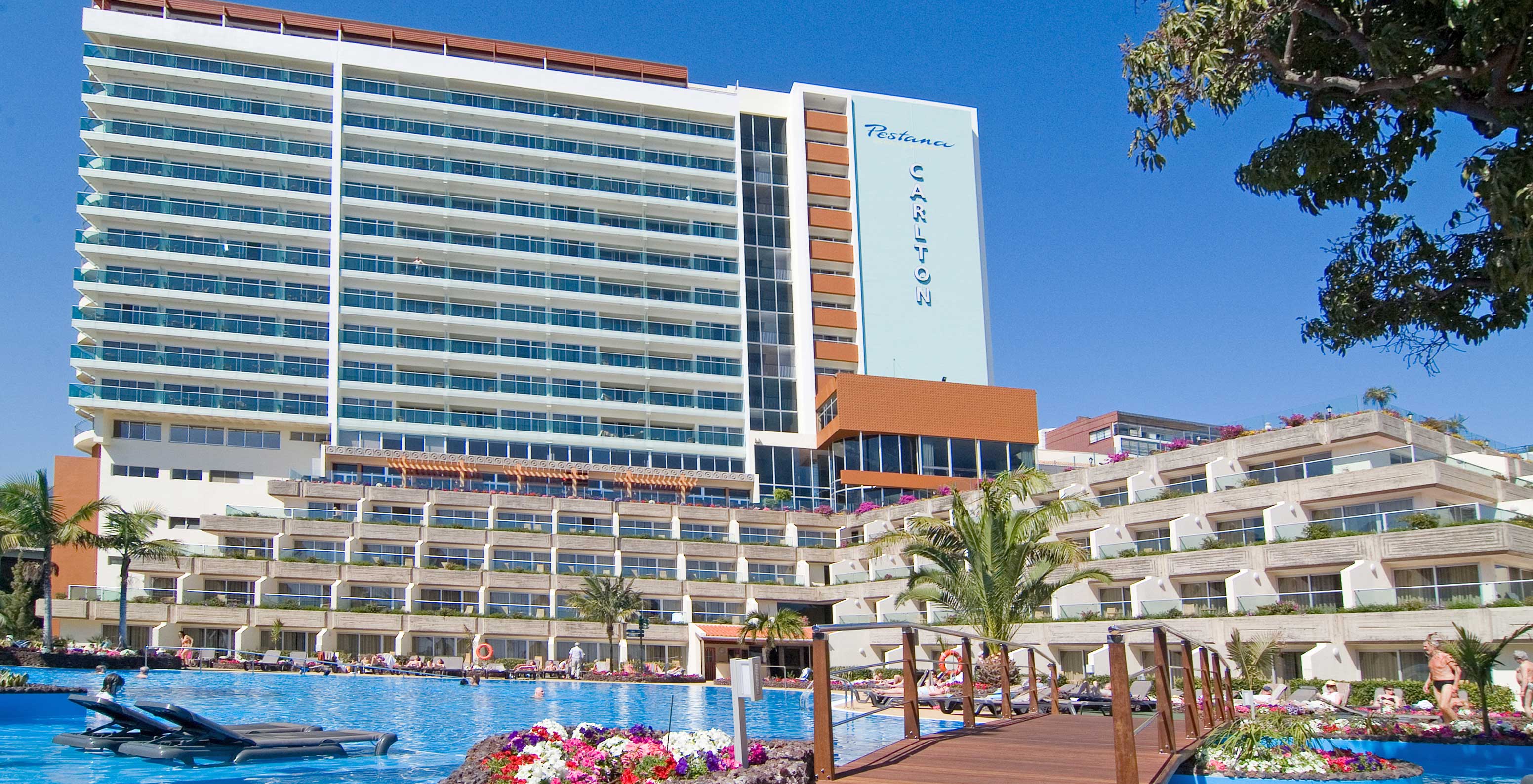 Vista da piscina do Pestana Carlton Madeira, com espreguiçadeiras na águas, e o edifício por trás