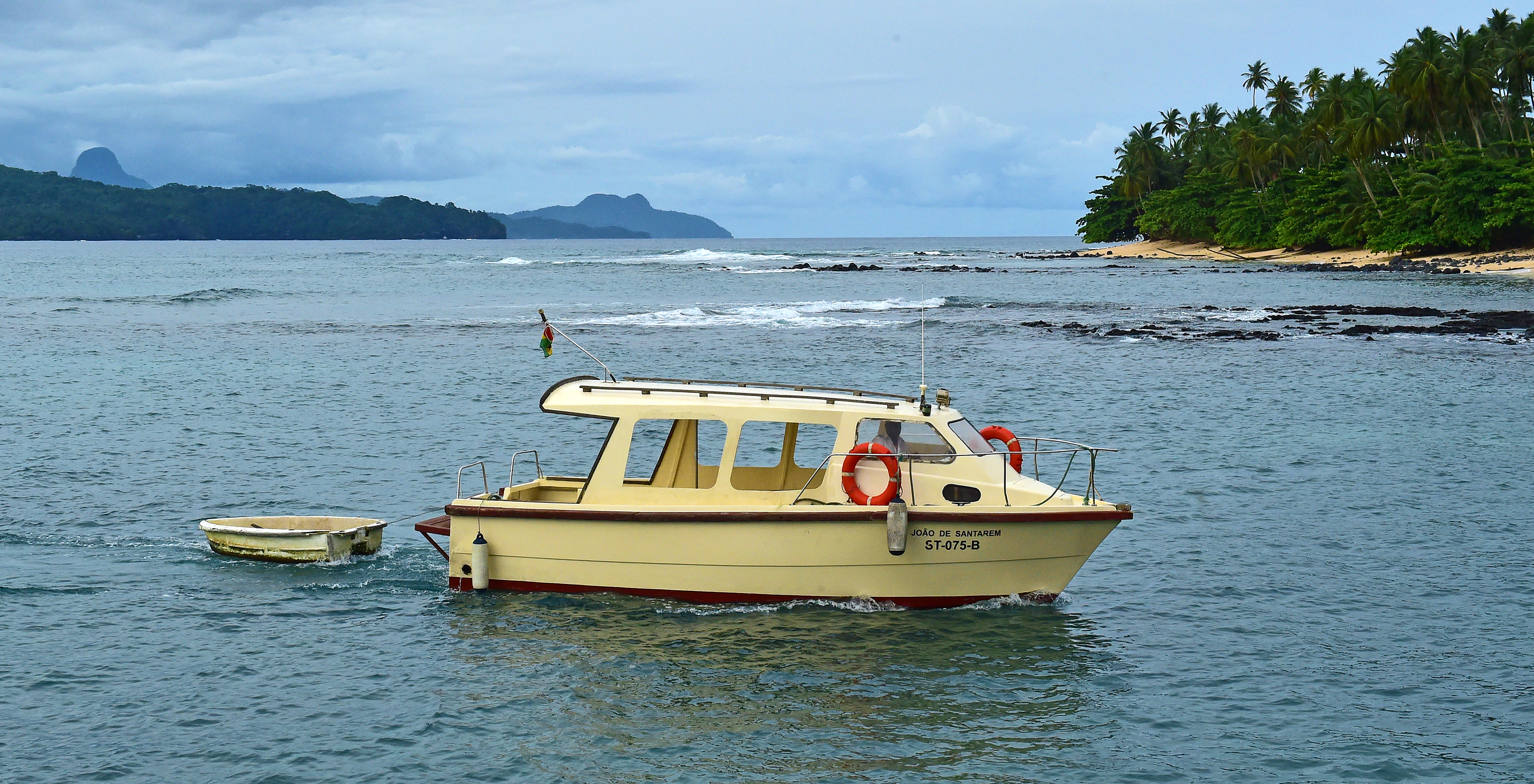 Barco de passeio com capacidade para algumas pessoas e com um mais pequeno atrelado, atracados perto da praia