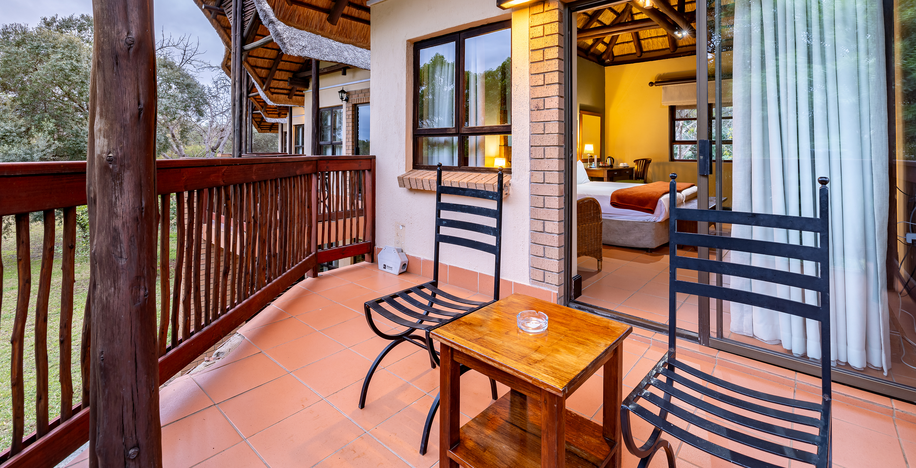 O Quarto Standard do Pestana Kruger Lodge tem uma varanda com detalhes em madeira, duas cadeiras e uma mesa de apoio