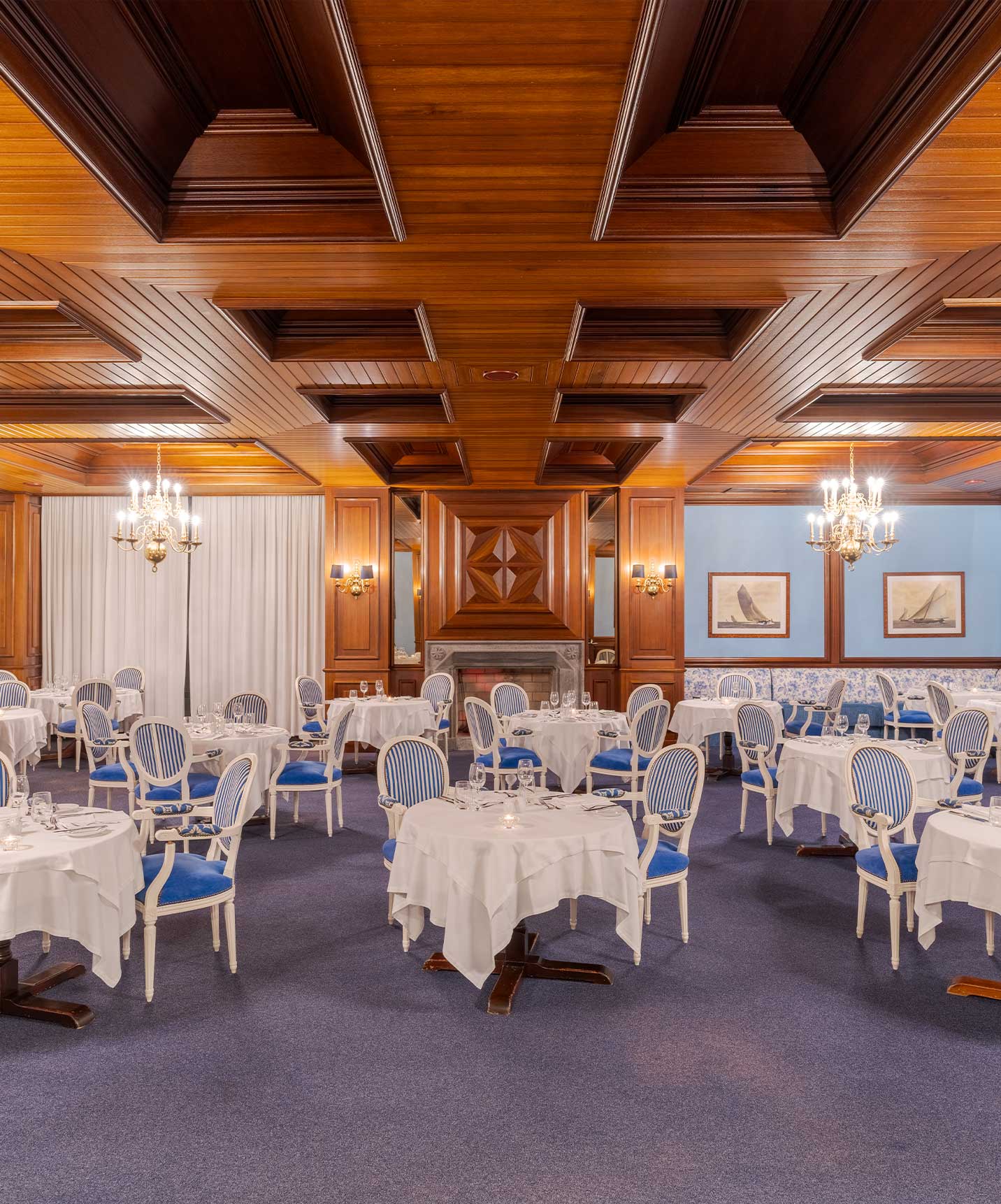 Parte interior do restaurante do Pestana Bahia Praia, com mesas de toalha branca, cadeiras azuis às riscas e teto de madeira