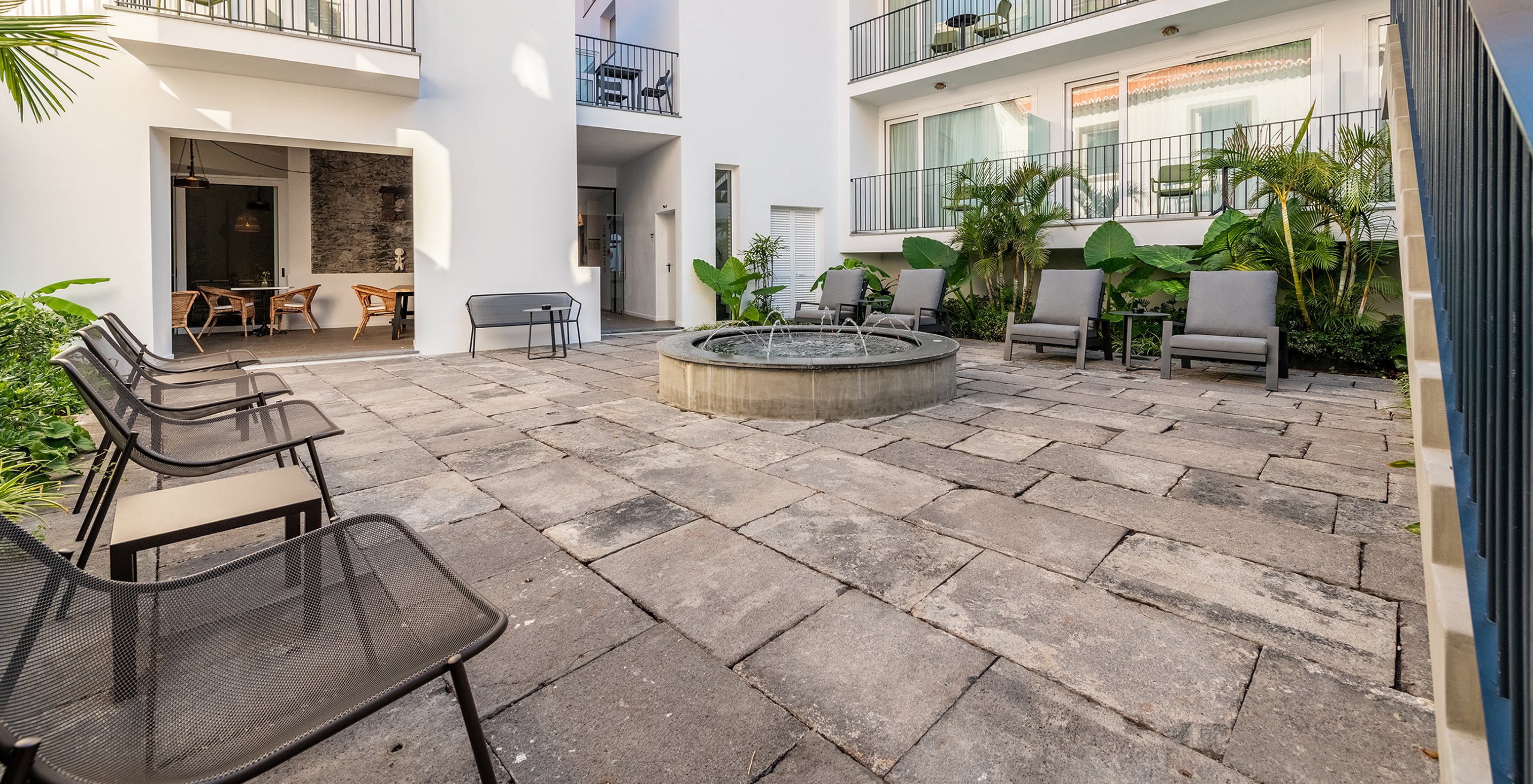 Pátio interior do Hotel em Câmara de Lobos, na Madeira, com várias plantas, varandas e uma esplanada